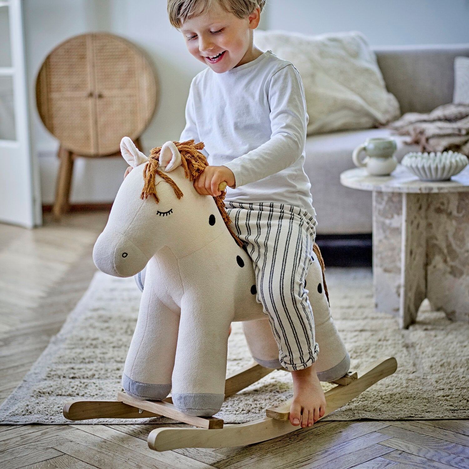 Schaukelpferd aus Plüsch, weißes Pferd mit brauner Mähne; Kind spielt auf Holzschaukel