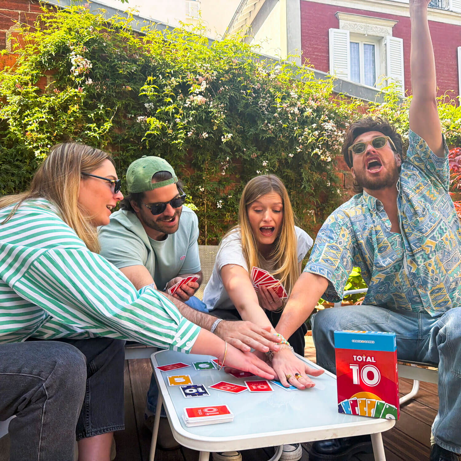 Gesellschaftsspiel Total 10 am Tisch: Karten und Schachtel, mehrere Spieler halten Spielkarten