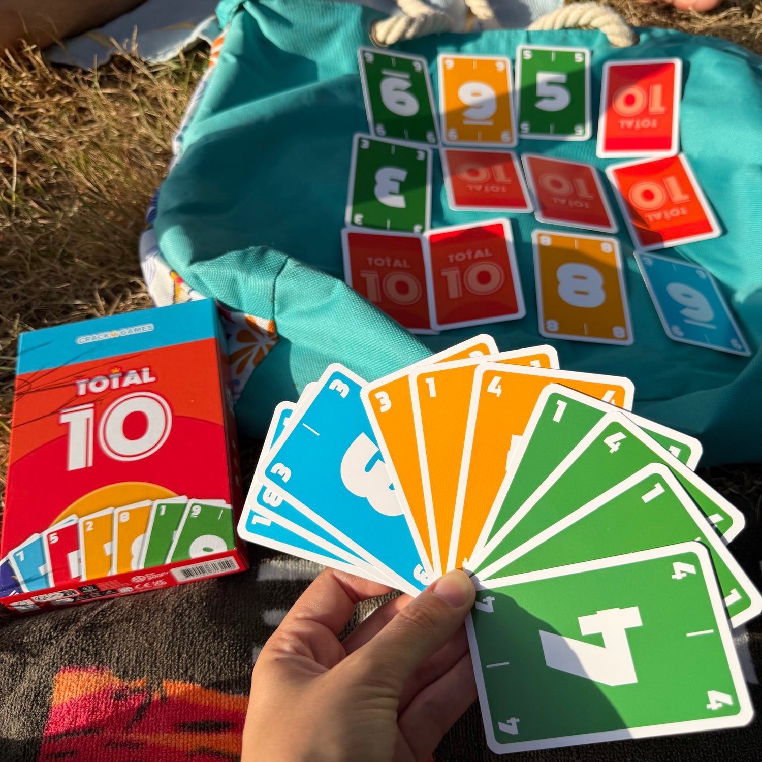 Spielkarten Total 10 in der Hand, Schachteln und bunte Karten auf Textilbeutel
