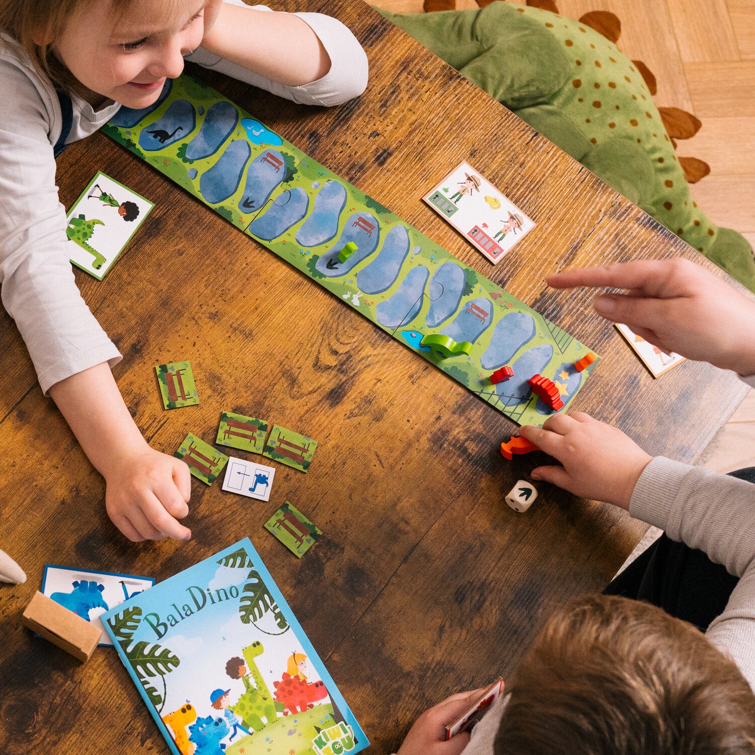 Dino-Spielset auf Holztisch: Kinder legen Karten auf eine Dino-Spielmatte