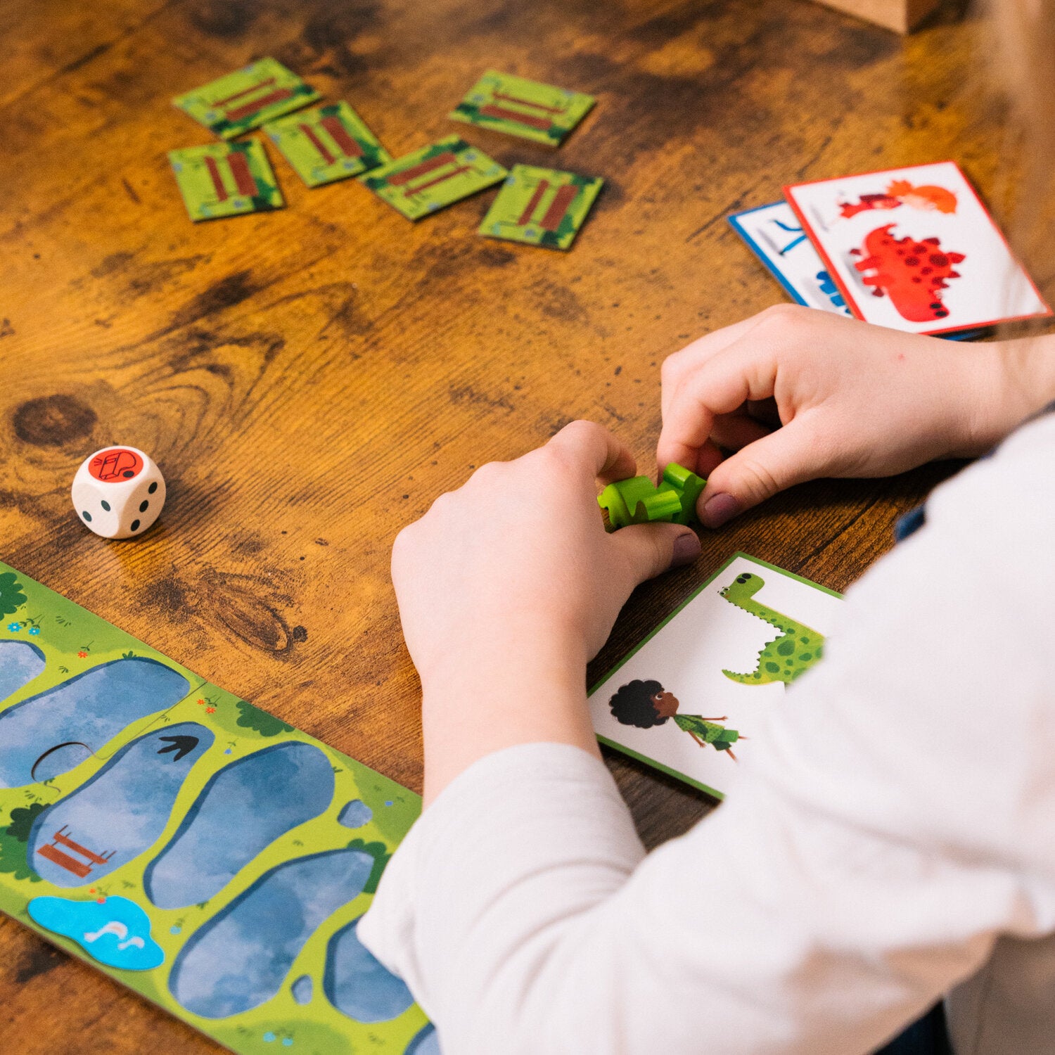 Dino-Spielsteine und Karten: Hände platzieren grüne Dinosaurierfiguren auf dem Brett