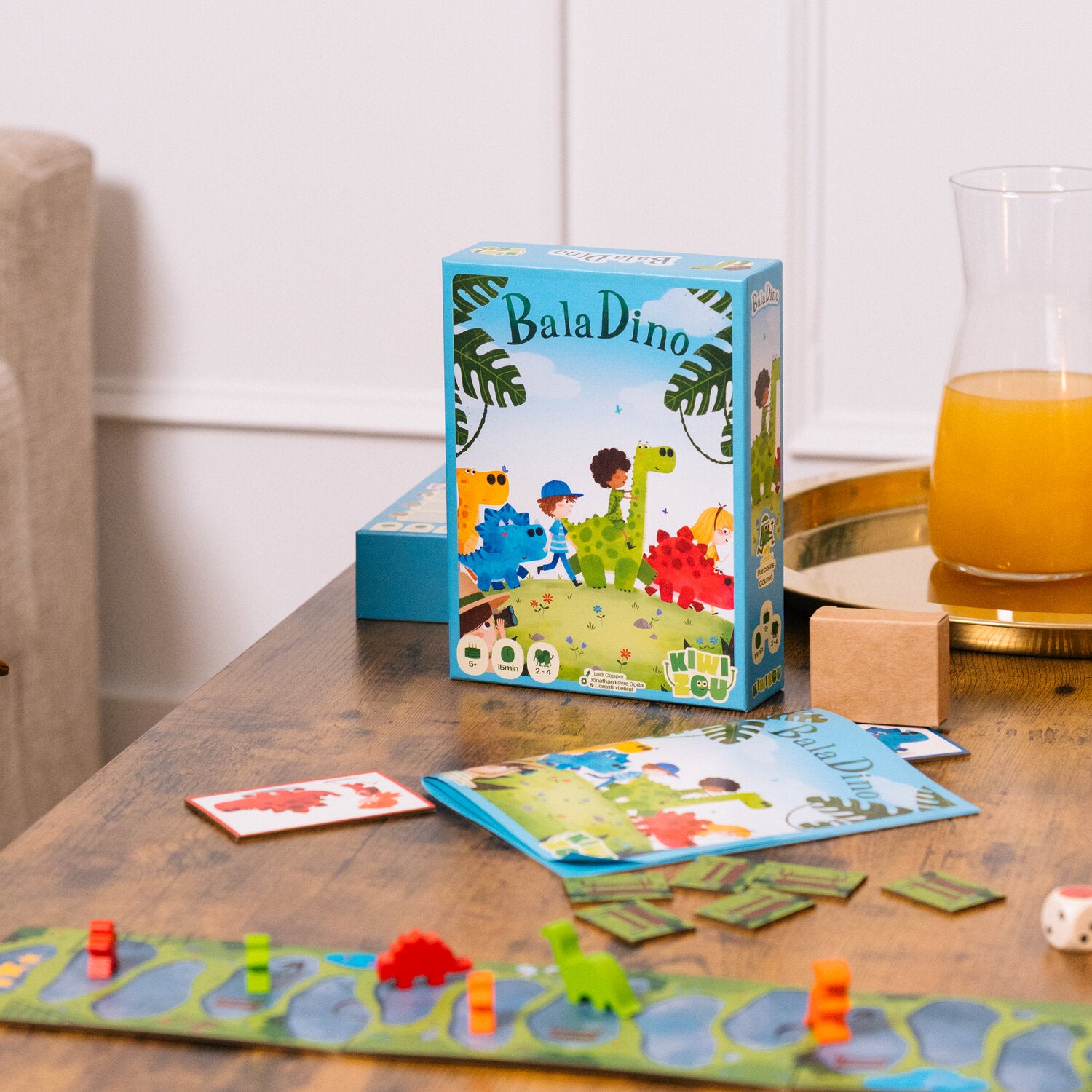 Dino-Brettspiel-Box auf Tisch, daneben Karten und zusammengefaltete Spielmatte