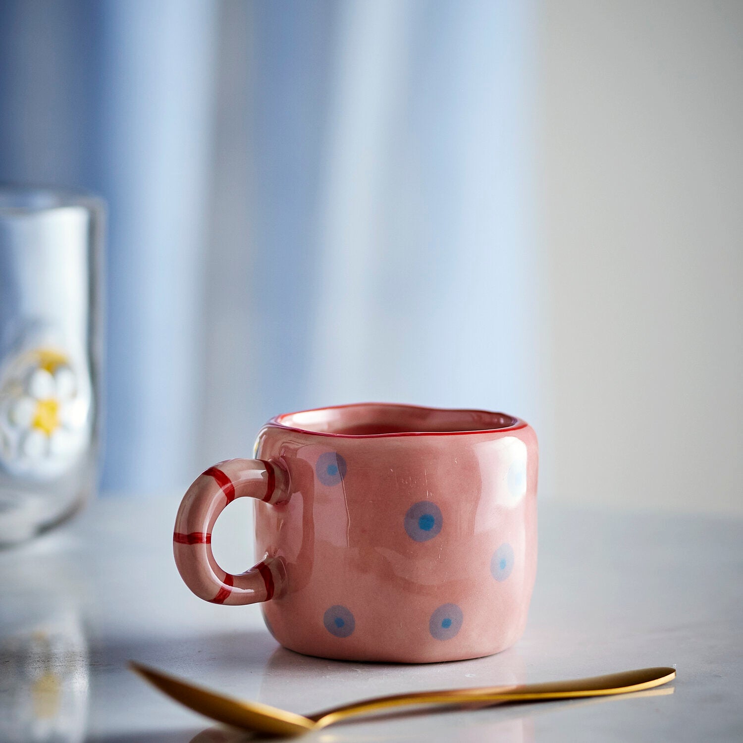 Rosa Tasse mit blauen Punkten und rot-weißem Ringhenkel, seitlicher Blick.
