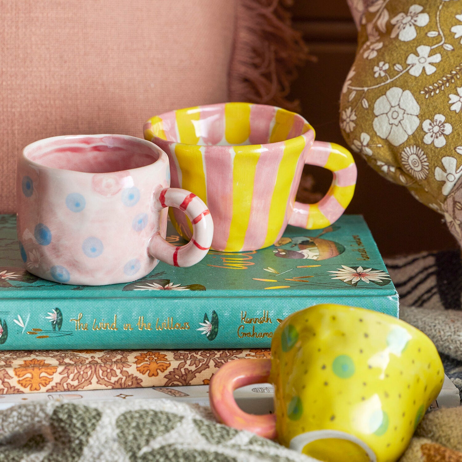 Rosa Tasse mit blauen Punkten und rot-weißem Henkel neben gelb-weißem Becher.