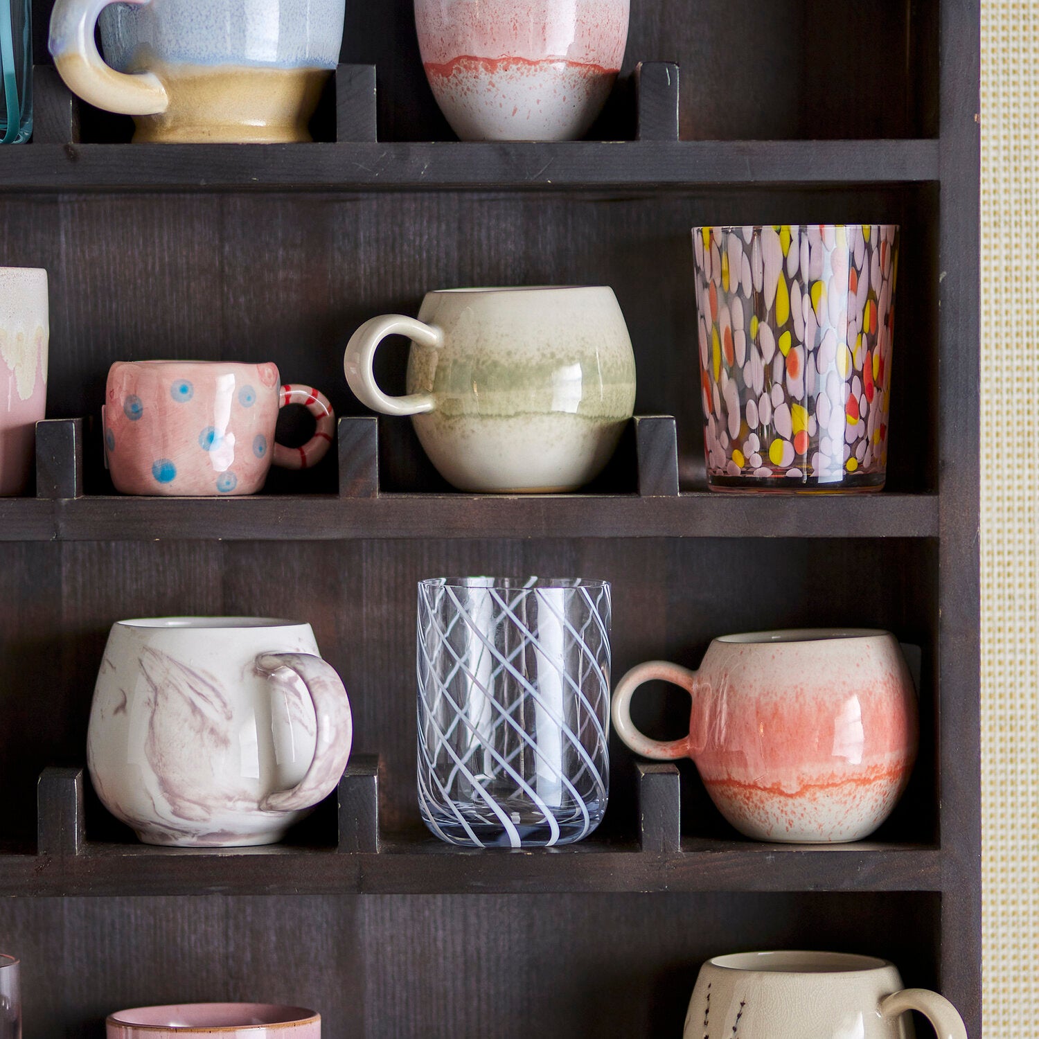 Rosa Tasse mit blauen Punkten und rot-weißem Henkel im Regal.