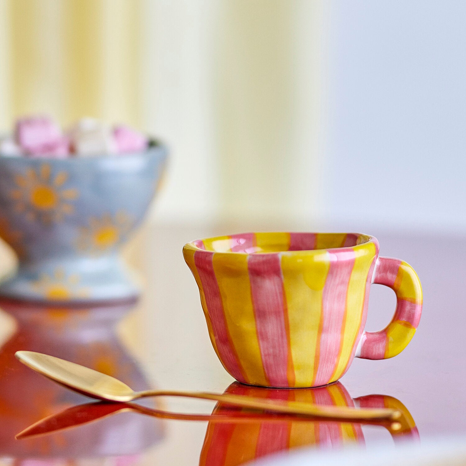 Gestreifte Tasse in Gelb und Rosa mit seitlichem Henkel in Seitenansicht.