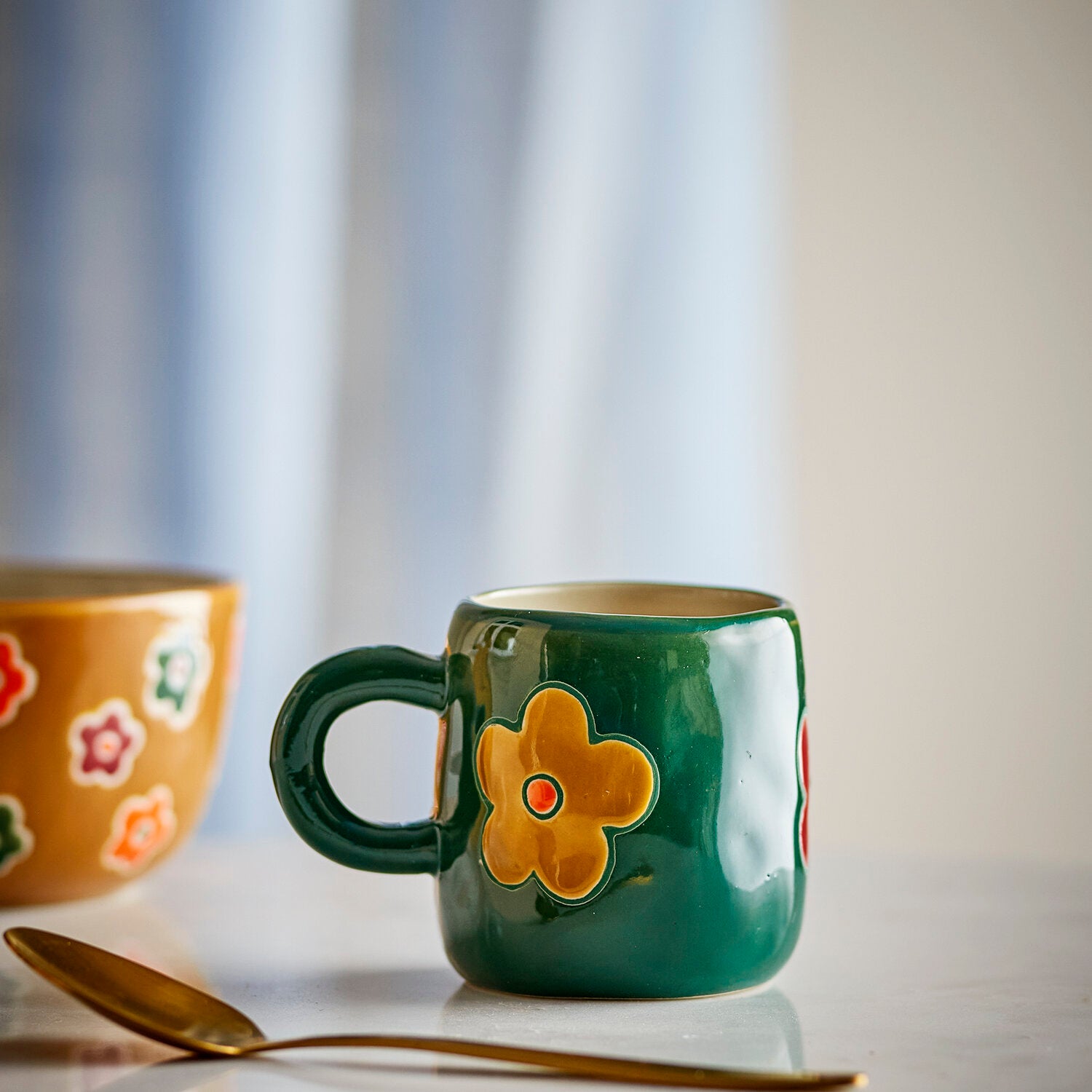 Dunkelgrüne Keramiktasse mit orangefarbener Blume und kurzem Henkel