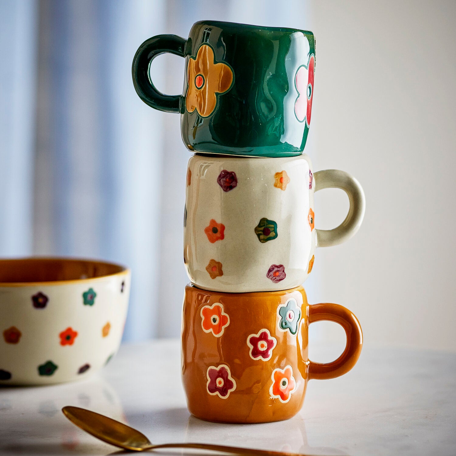 Dunkelgrüne Keramiktasse mit orangefarbener Blume, gestapelt auf weiteren Tassen
