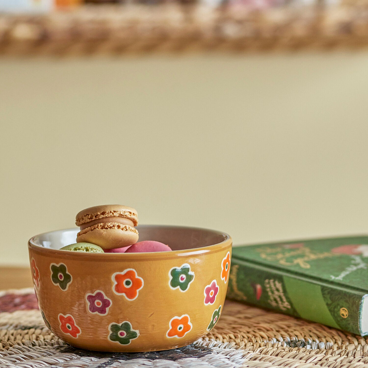 Braune Schale mit bunten Blümchen, gefüllt mit Macarons auf Strohnest
