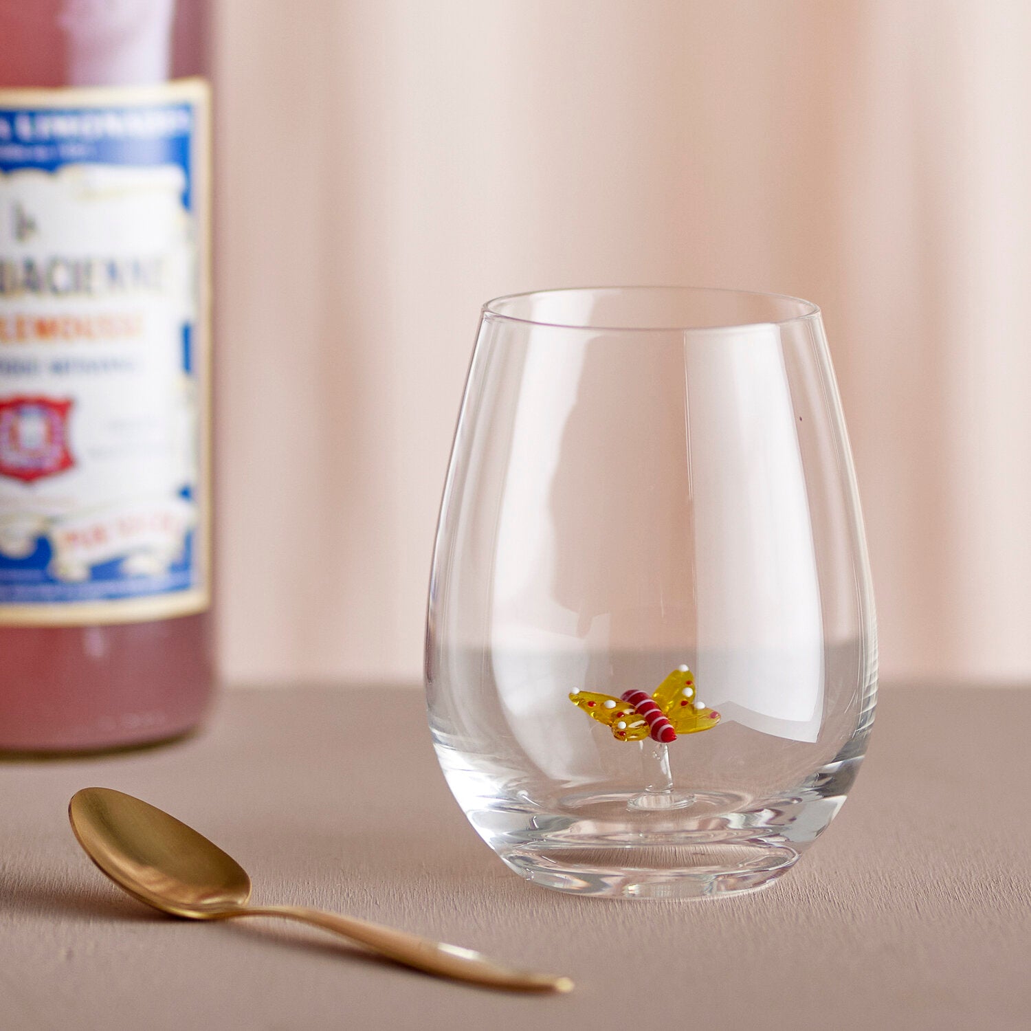 Kleines klares Trinkglas mit Schmetterlingsdekor auf flacher Fläche