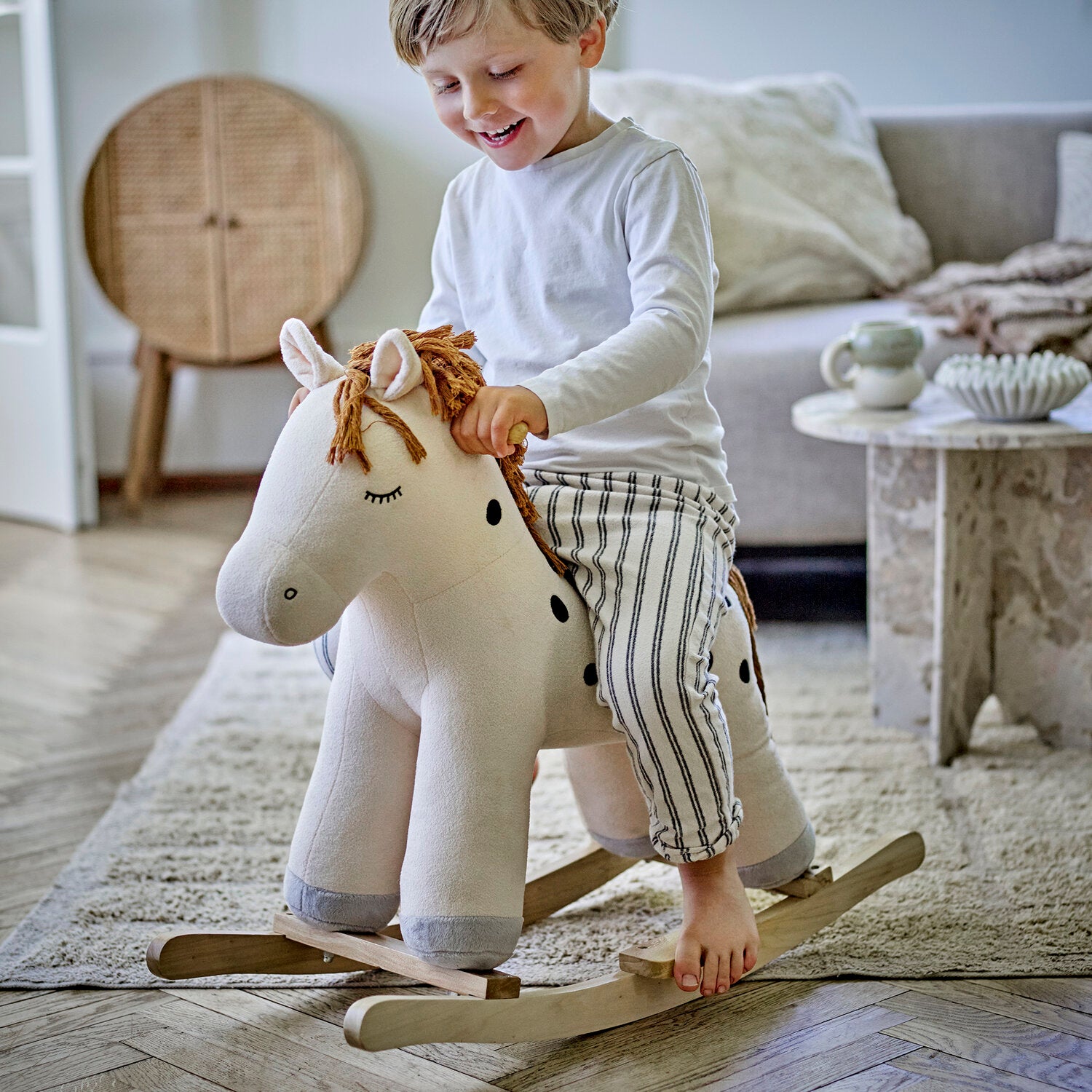 Schaukelpferd aus Plüsch, weißes Pferd mit brauner Mähne; Kind spielt auf Holzschaukel