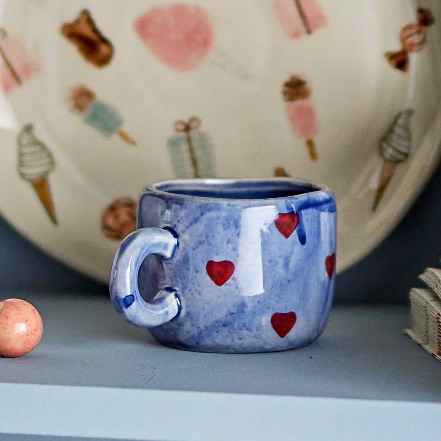 Blaue Tasse mit Herzmuster und großem Henkel, auf liegender Fläche