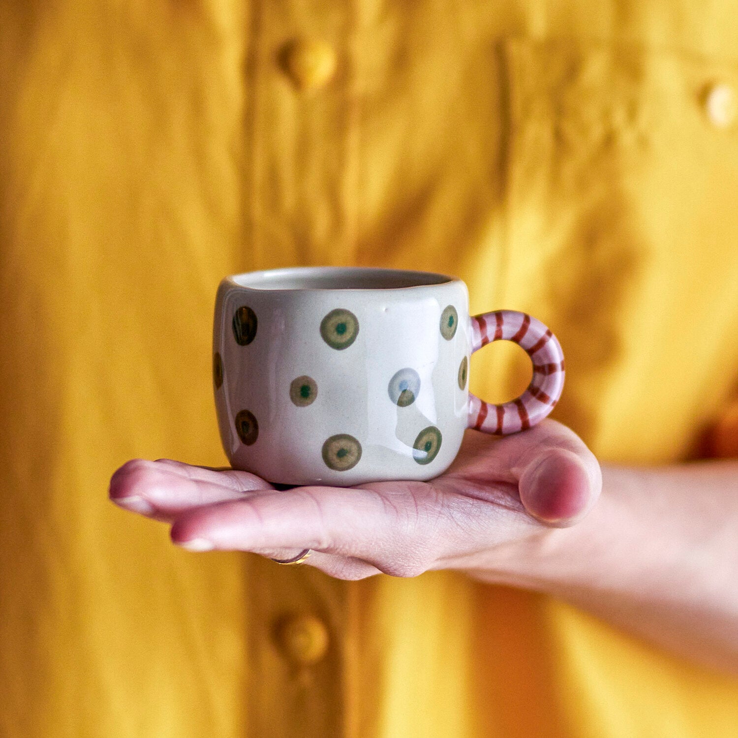 Hand hält Tasse mit Punkten in Natur und gestreiftem Ringhenkel