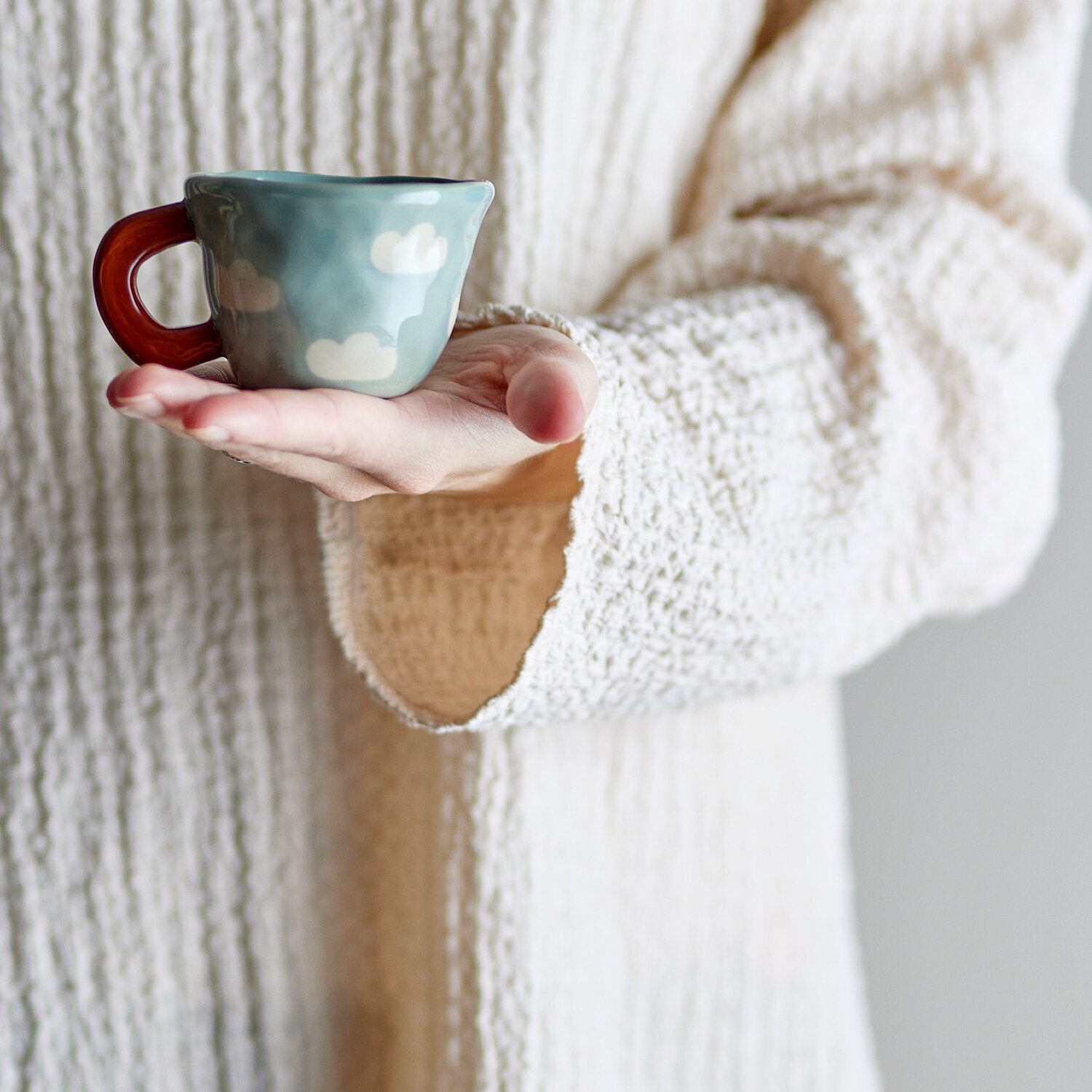 Blaue Tasse mit Wolkenmuster und rotem Henkel in einer Hand