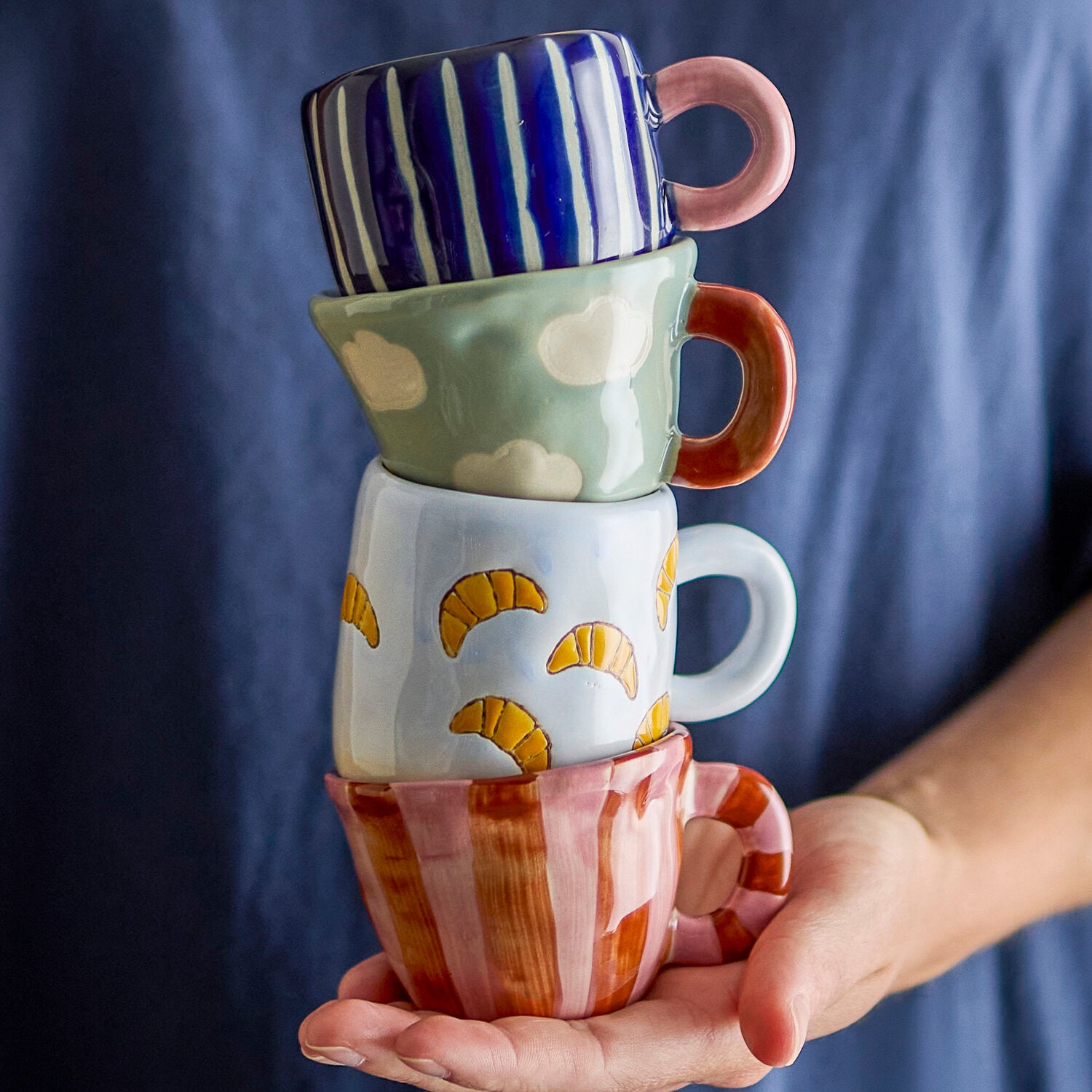 Blaue Tasse mit Wolkenmuster und rotem Henkel in Hand gehalten