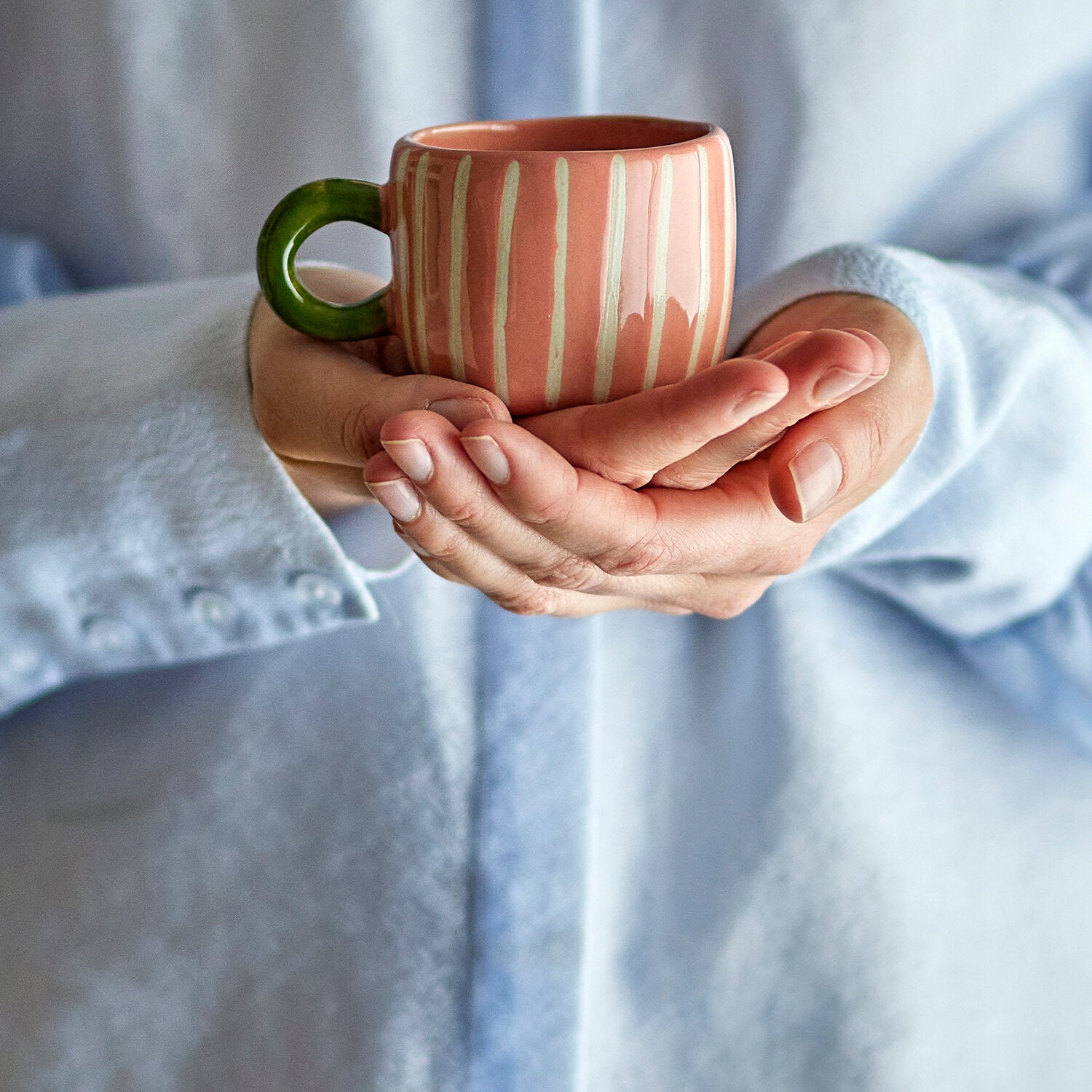 Rosa Tasse mit weißen Streifen und grünem Henkel in Händen, Keramikbecher