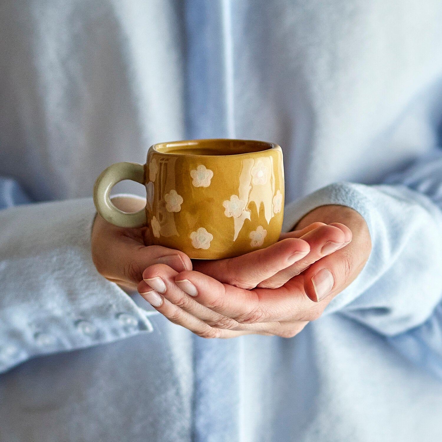 Braune Tasse mit weißem Blumenmuster, in den Händen gehalten, mit stabilem Henkel