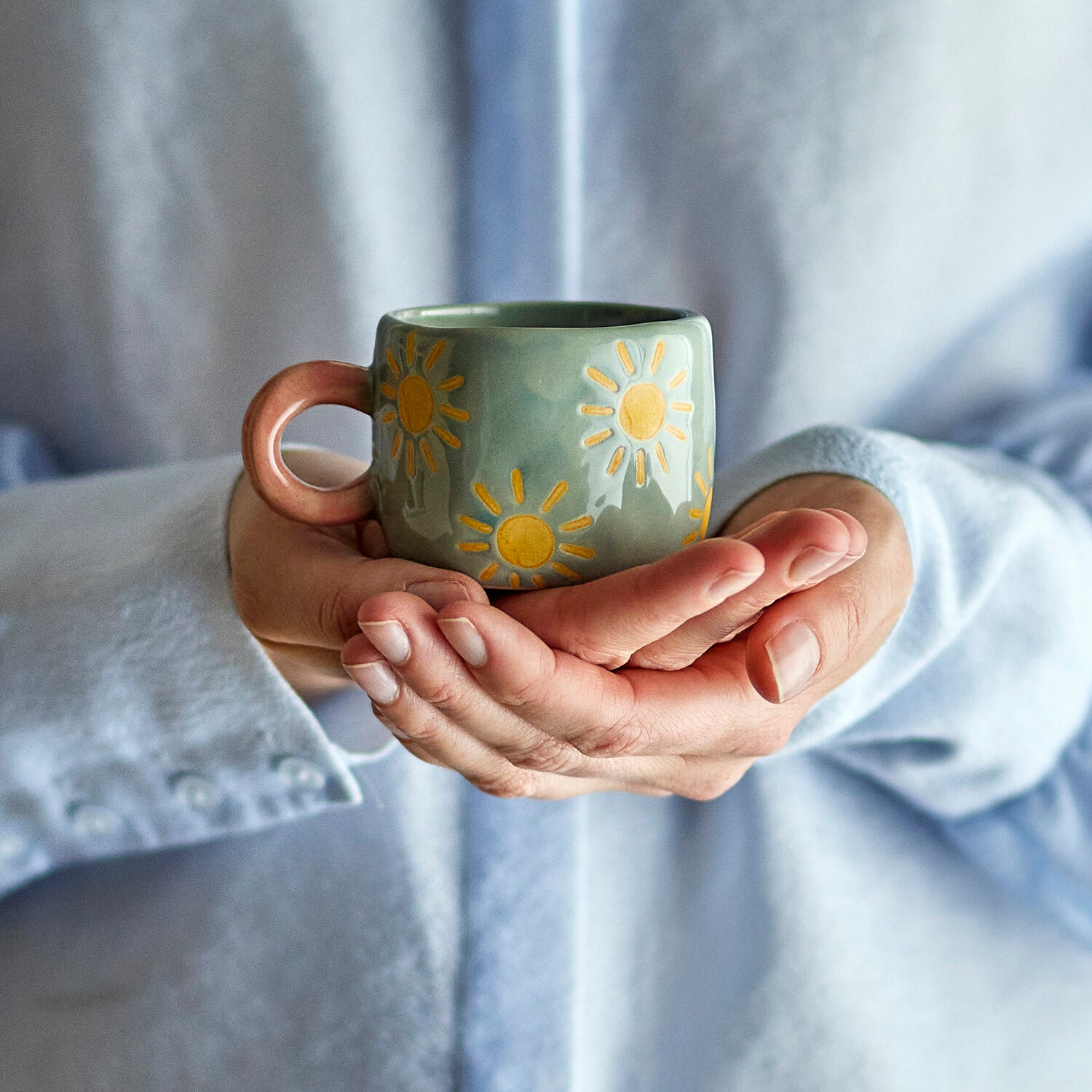 Grün-graue Tasse mit Sonnenmotiv, rosafarbenem Henkel in den Händen