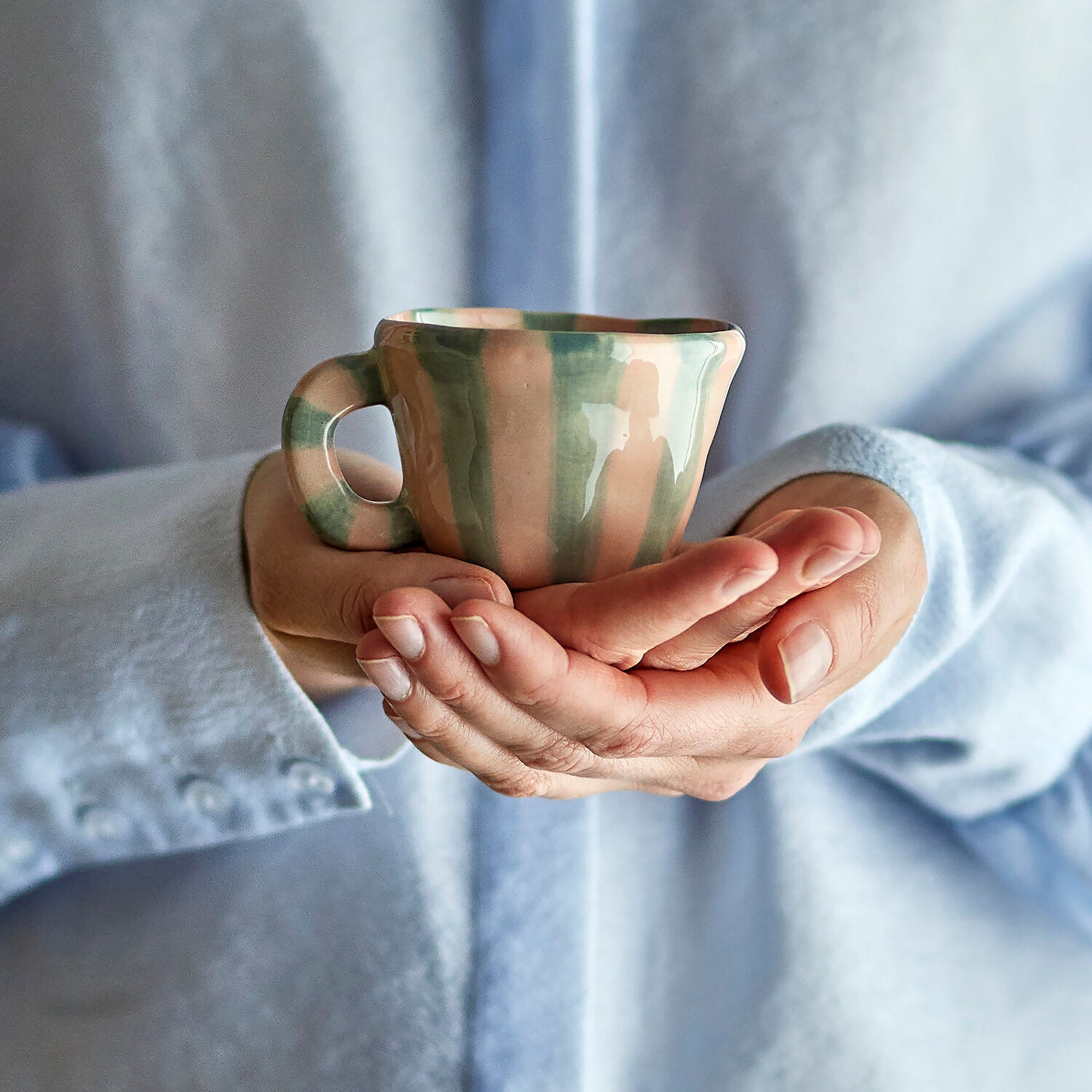 Tasse „Nini“ mit rosa- und graugrünen Streifen in Händen, Blick frontal
