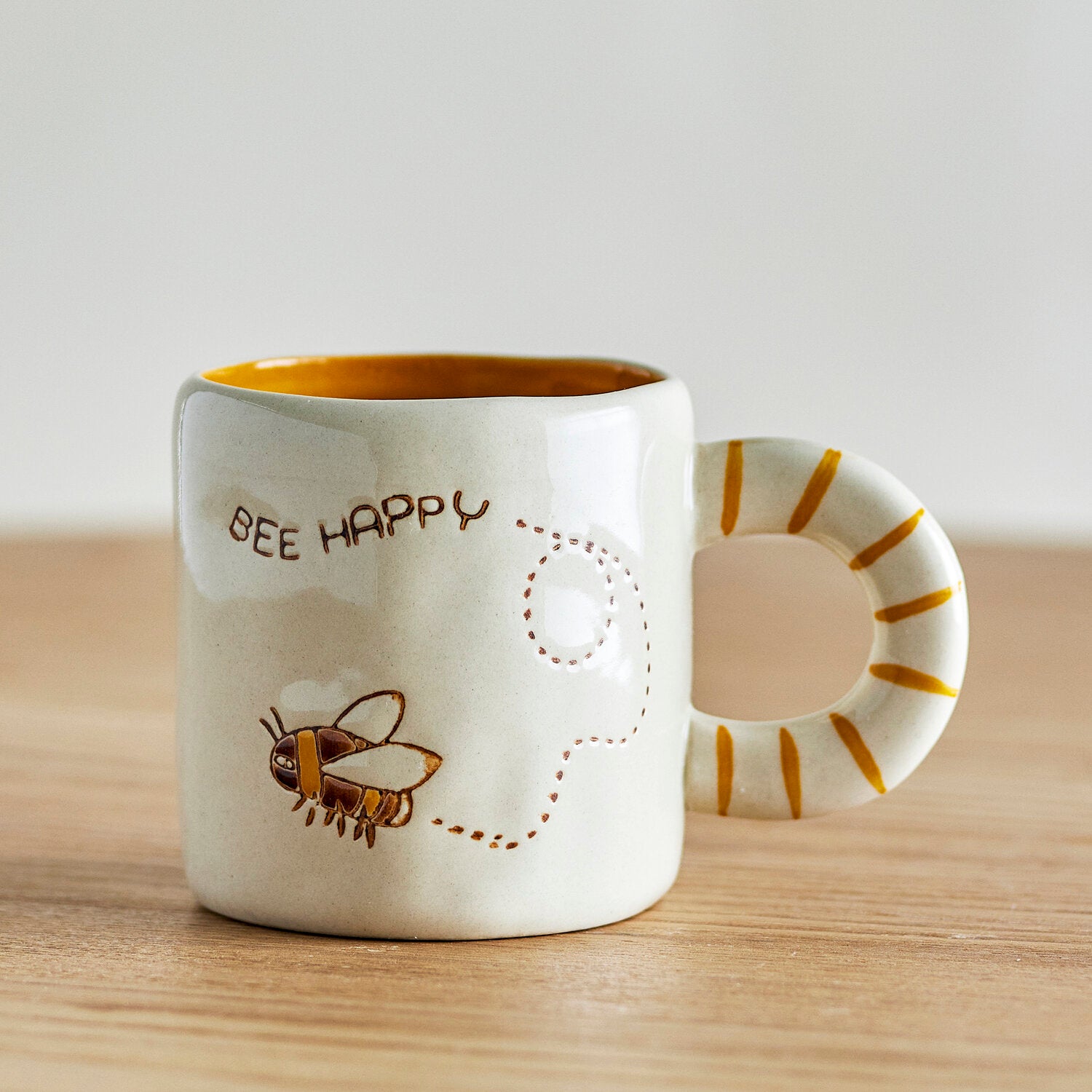 Naturfarbene Tasse mit „BEE HAPPY“-Aufdruck, Bienenillustration und gestreiftem Henkel
