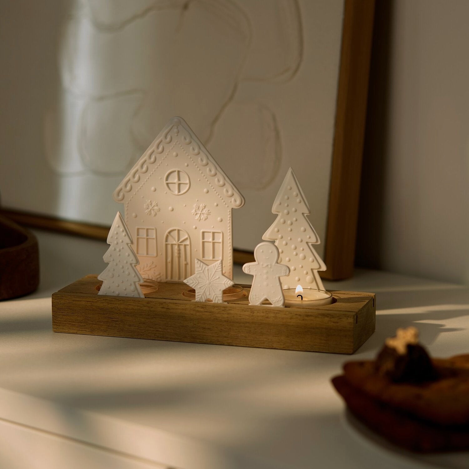 Lichtszene auf Holzsockel mit weißem Haus und Tannen, warm beleuchtete Teelichter