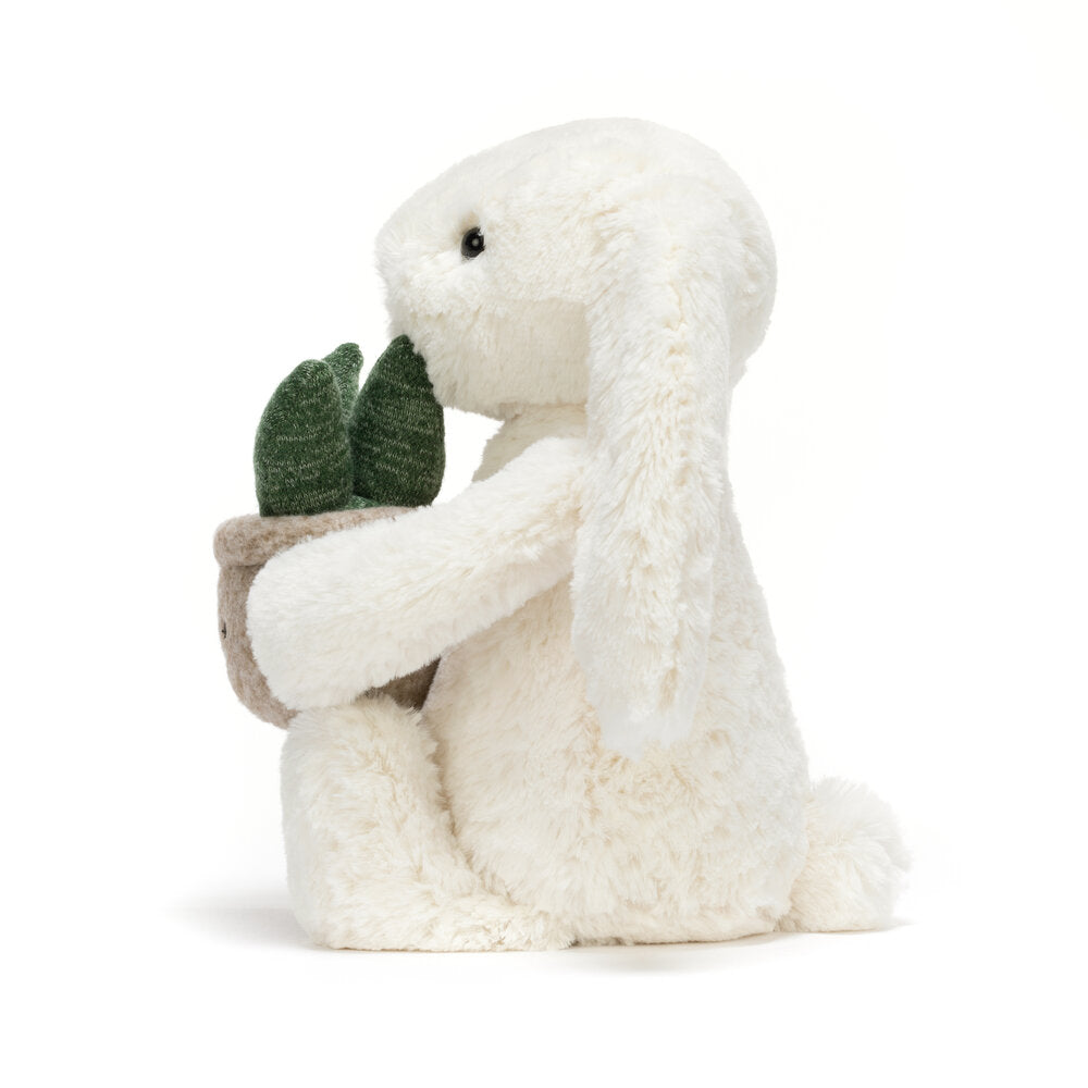 Kuscheltierhase in Creme in Seitenansicht, hält Pflanzentopf mit grünen Blättern