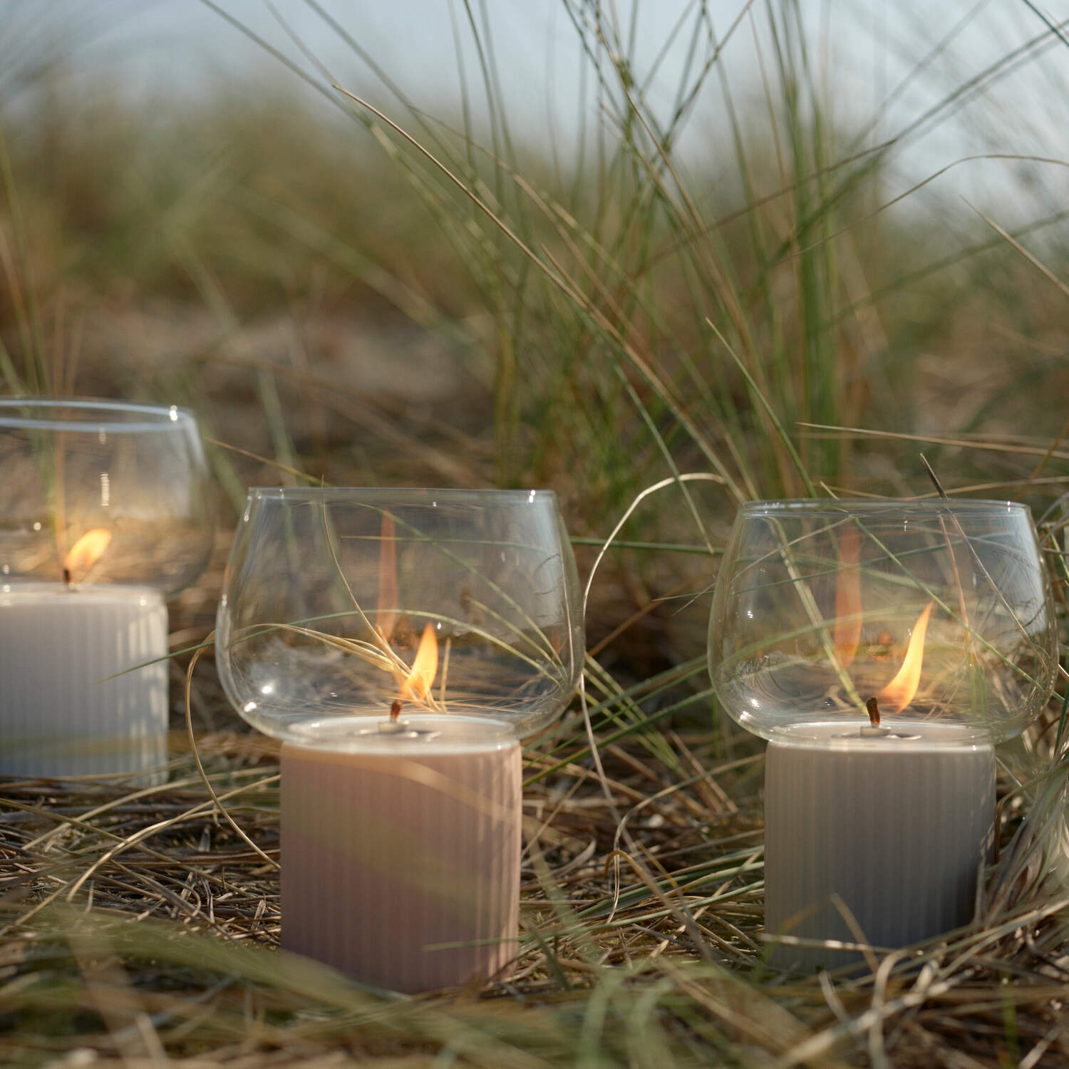 Windlicht HYGGE mit Glaszylinder auf geriffeltem rosa Sockel, im Gras aufgestellt