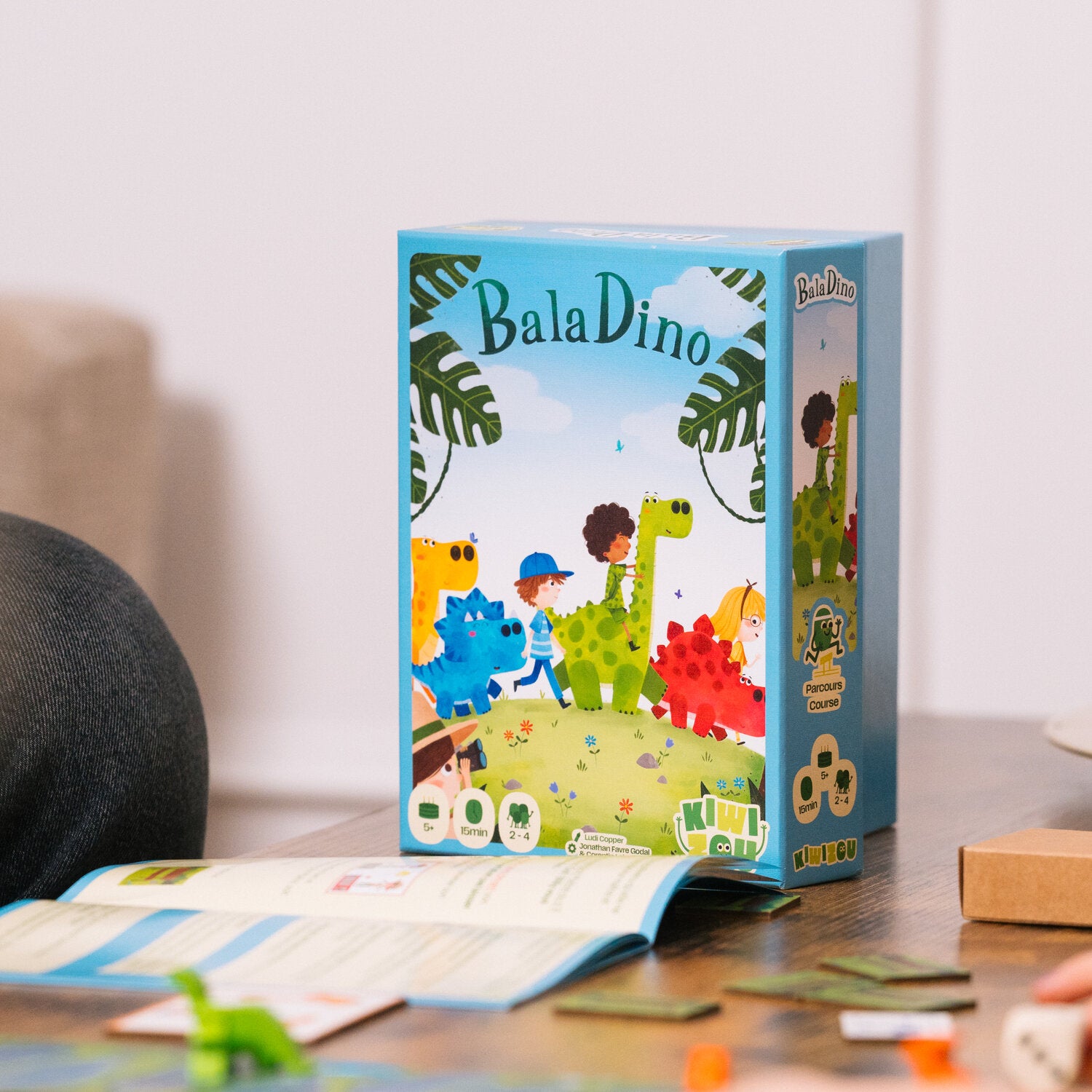 BalaDino Spielbox auf dem Tisch, daneben Spielkarten und Teile des Brettspiels