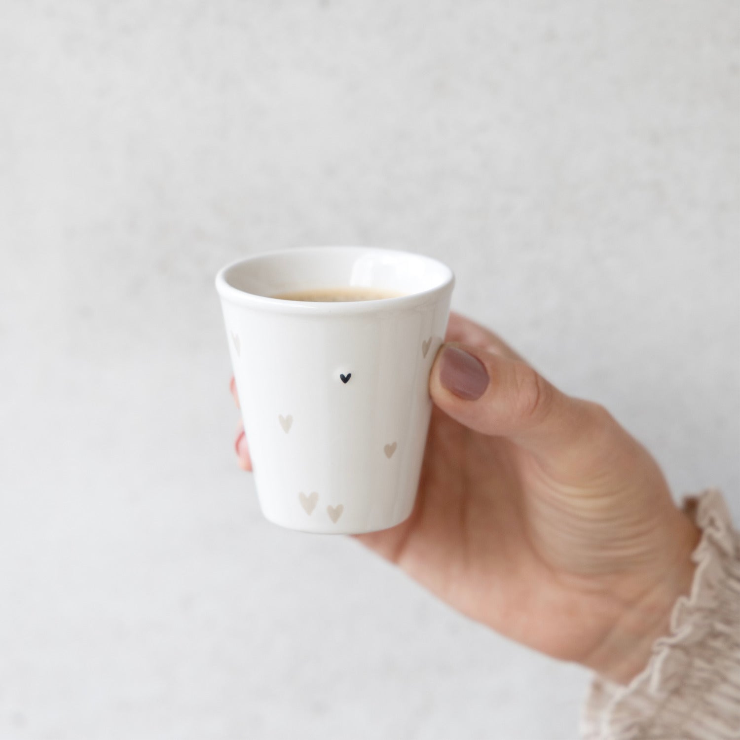 Weißer Becher mit schwarzen Herzchen, in Hand gehalten