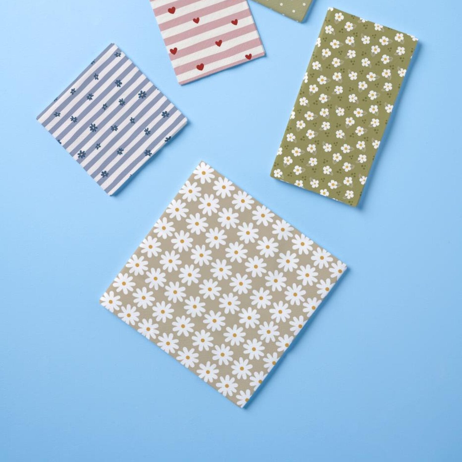 Mehrere quadratische Papierservietten, eine mit weißen Margeriten auf beige