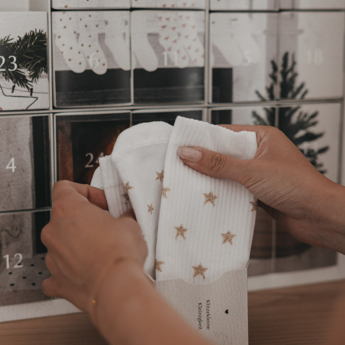 Socken-Adventskalender, Hände entnehmen weiße Socken mit goldenen Sternen aus Box
