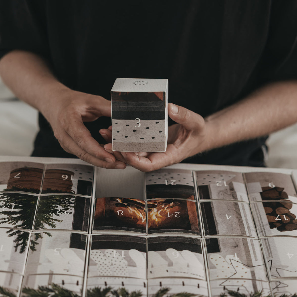 Adventskalender mit Socken: offene Box mit nummerierten Fächern, Hände halten ein kleines Teil