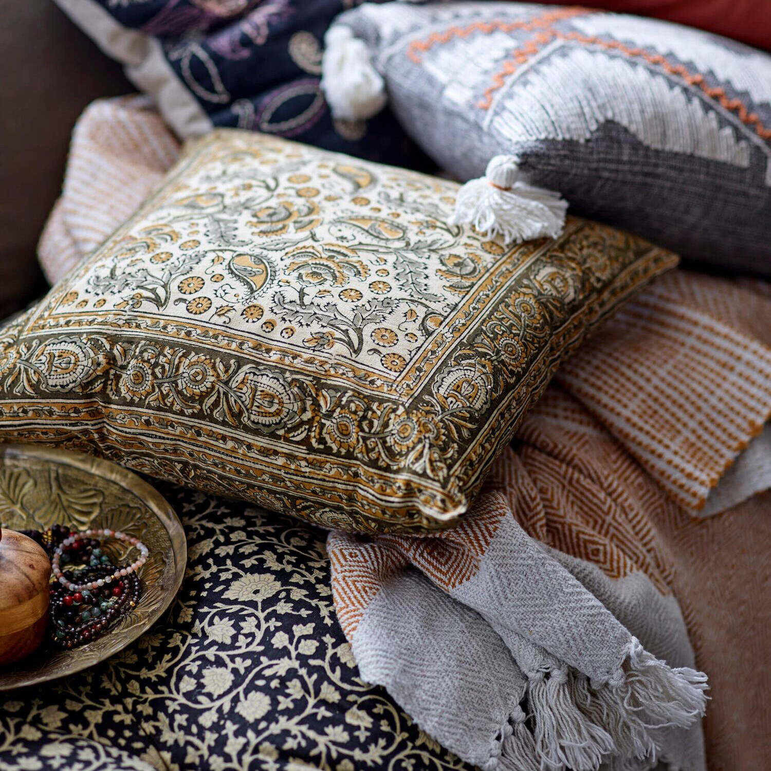 Goldfarbenes Tablett auf Decke mit Paisley-Muster, Quaste und Deko