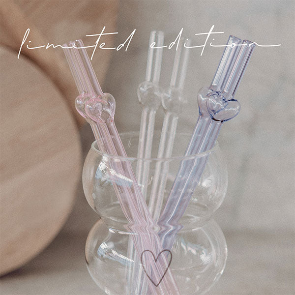 Drei Glasstrohhalme mit Herzaufsatz im Becher: transparent, rosa und flieder