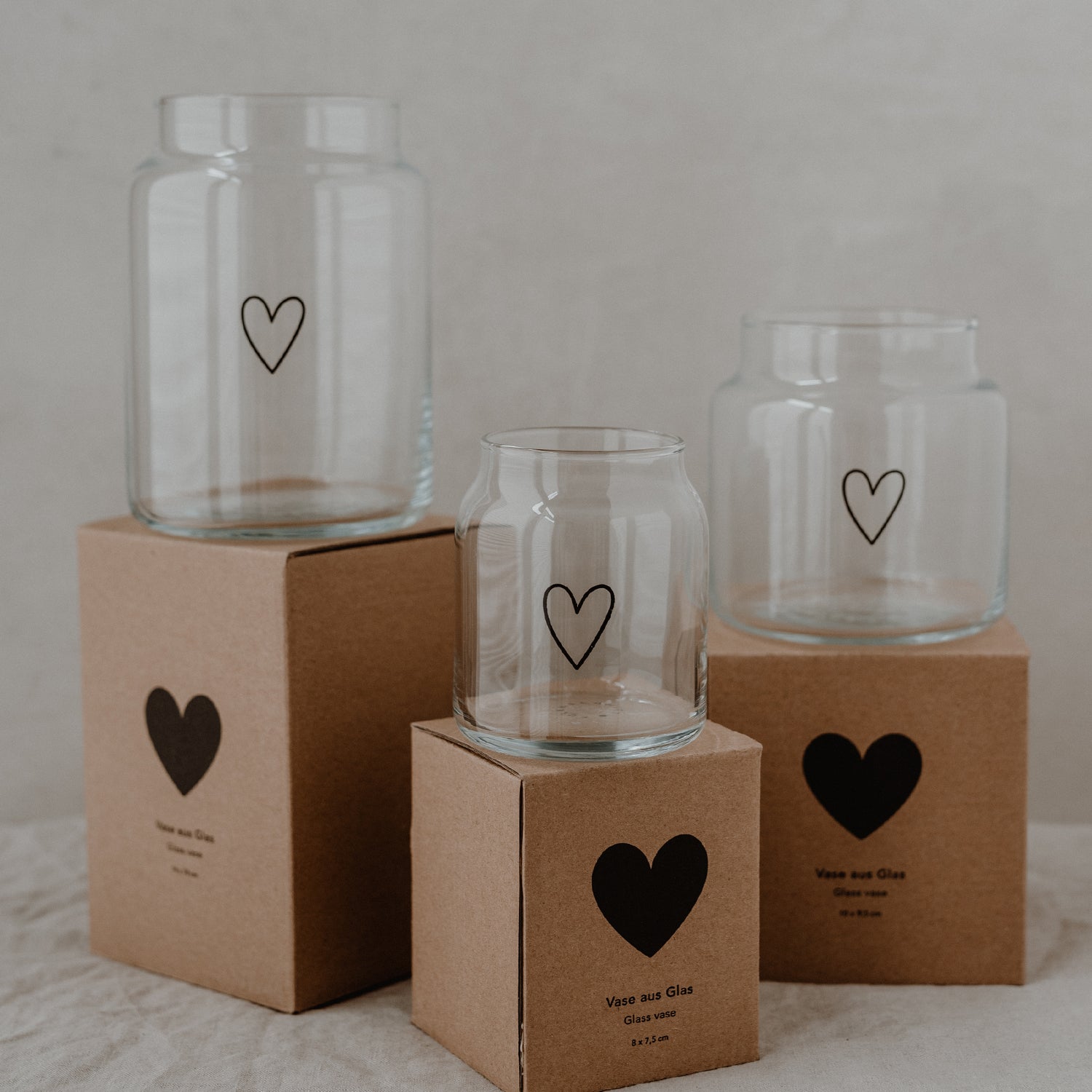 Drei transparente Glasvasen mit Herzsymbolen auf Geschenkboxen