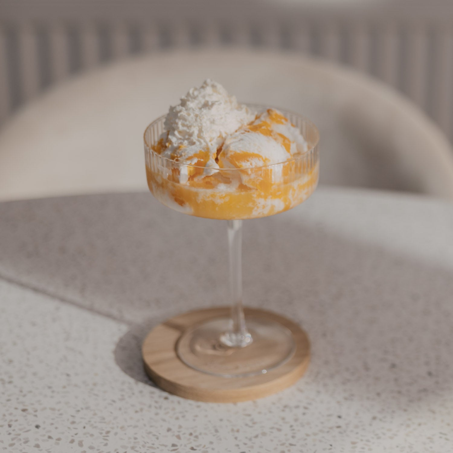 Champagnerglas auf Holzuntersetzer, gefüllt mit Orangencocktail und Eis