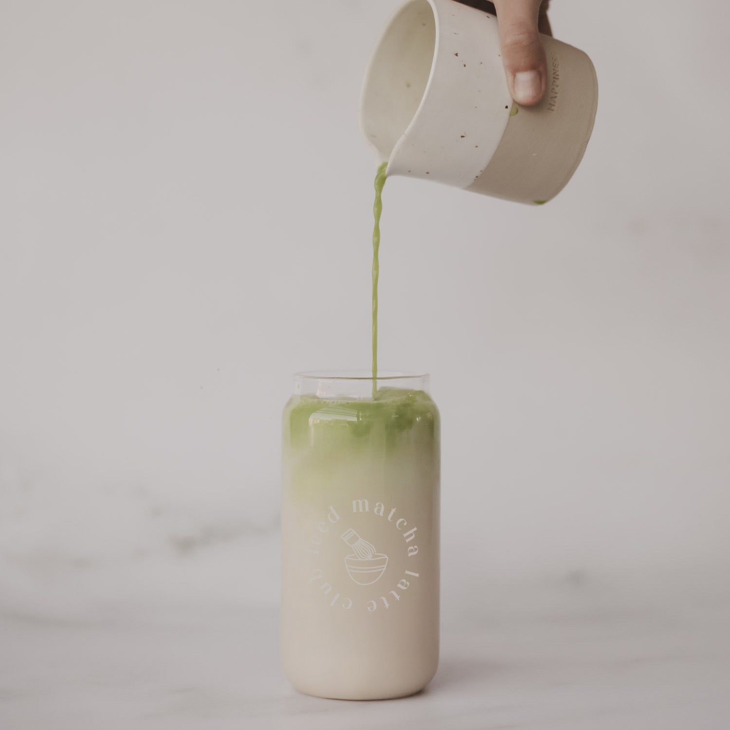 Trinkglas mit Schrift „iced matcha latte club“, Milchgetränk im Glas beim Eingießen