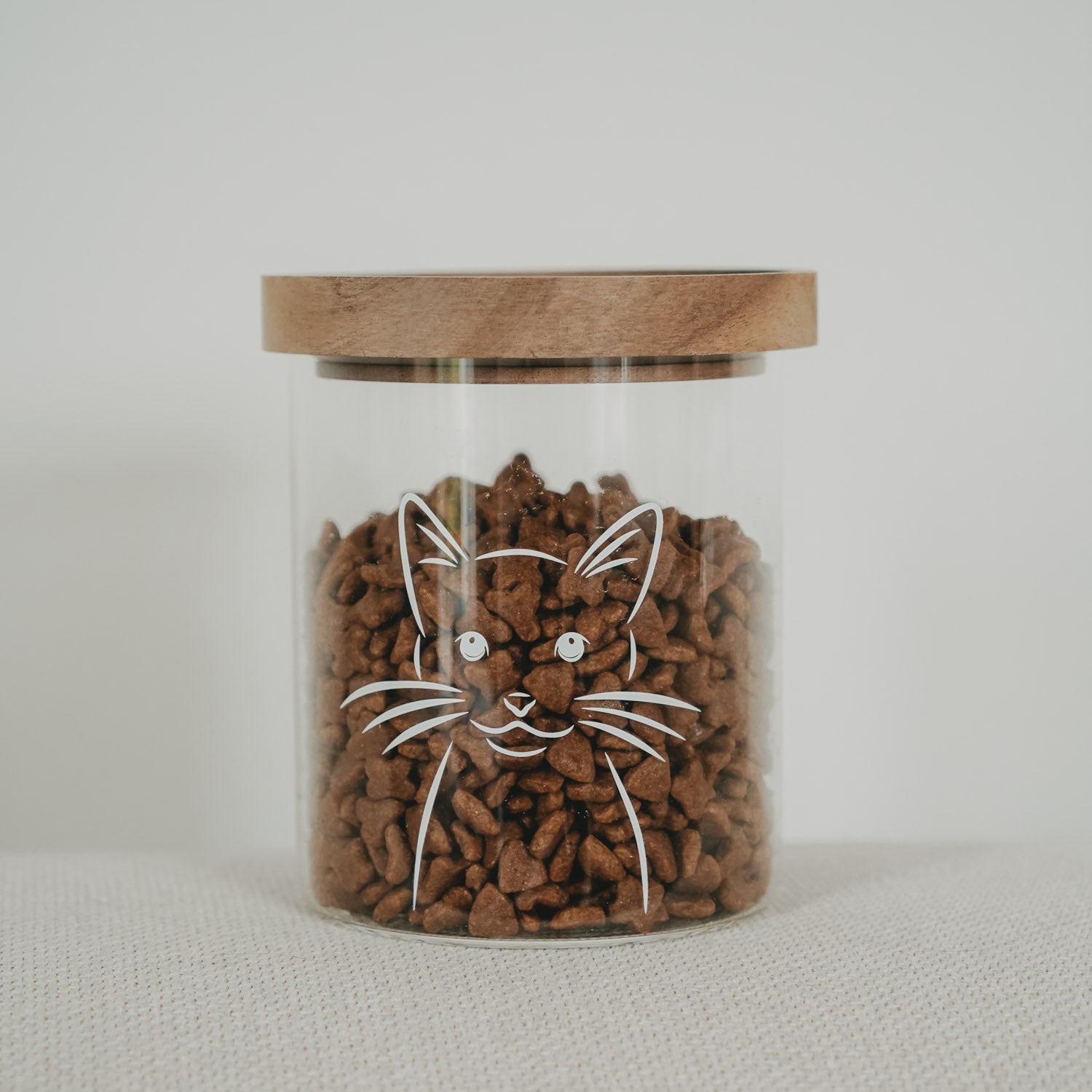 Vorratsglas mit Katzenmotiv, klarer Behälter und Holzdeckel, gefüllt mit braunen Kroketten