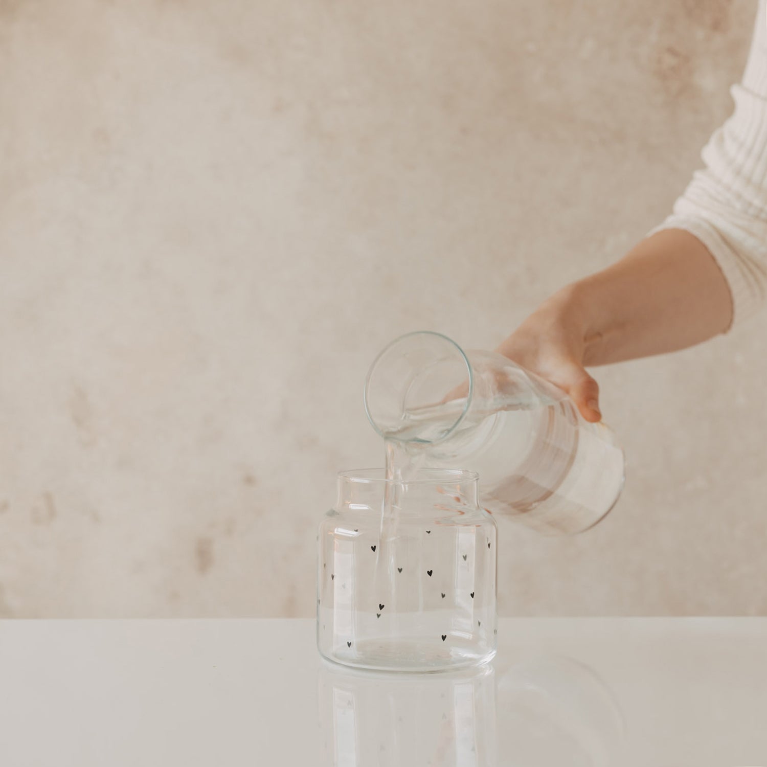 Glasvase mit Herzmotiven, Hand gießt Wasser in die Öffnung
