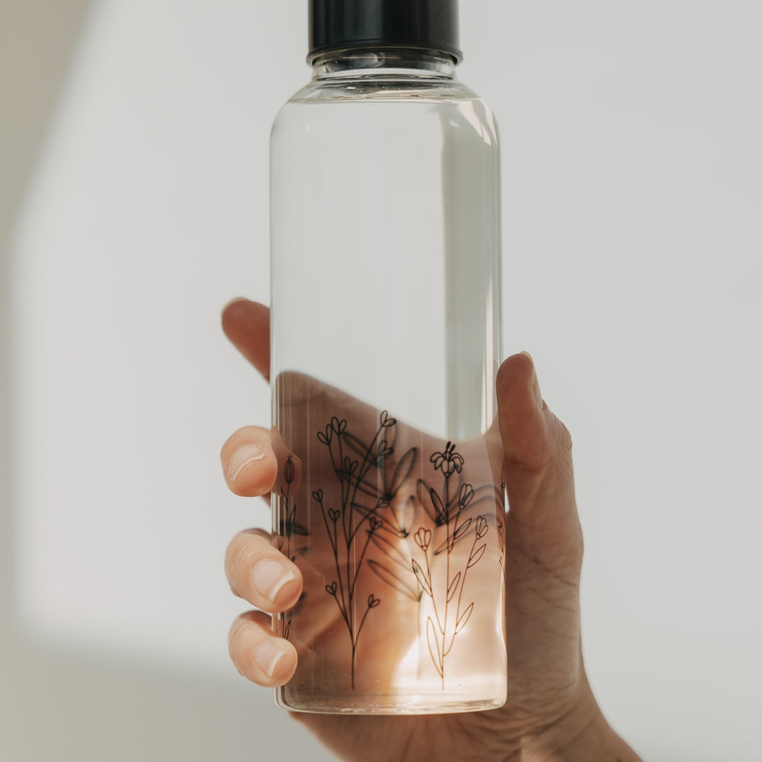 Transparente Trinkflasche 500 ml mit Blumenwiesen-Motiv, in der Hand gehalten