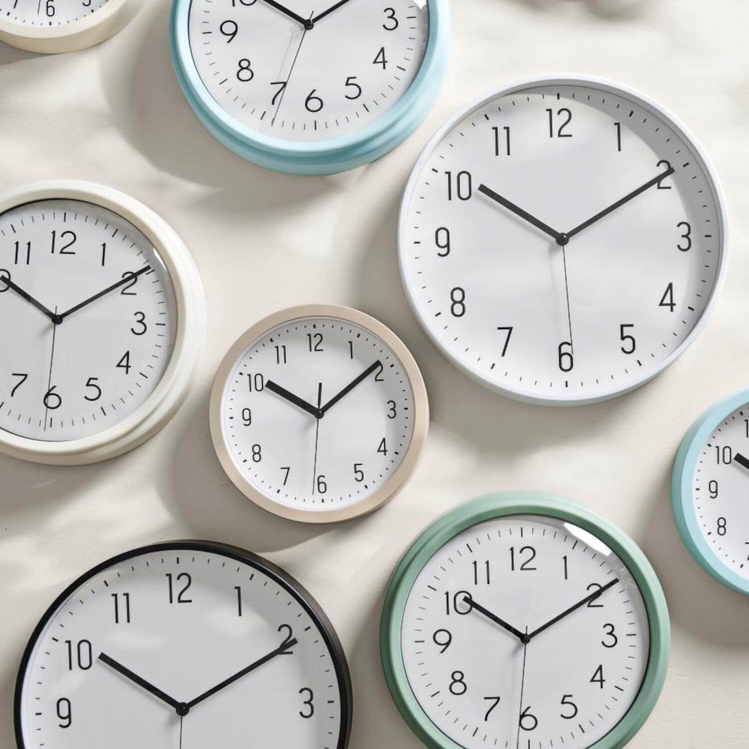 Mehrere Wanduhr-Modelle mit weißen Ziffernblättern und schwarzen Zeigern, grün und blau