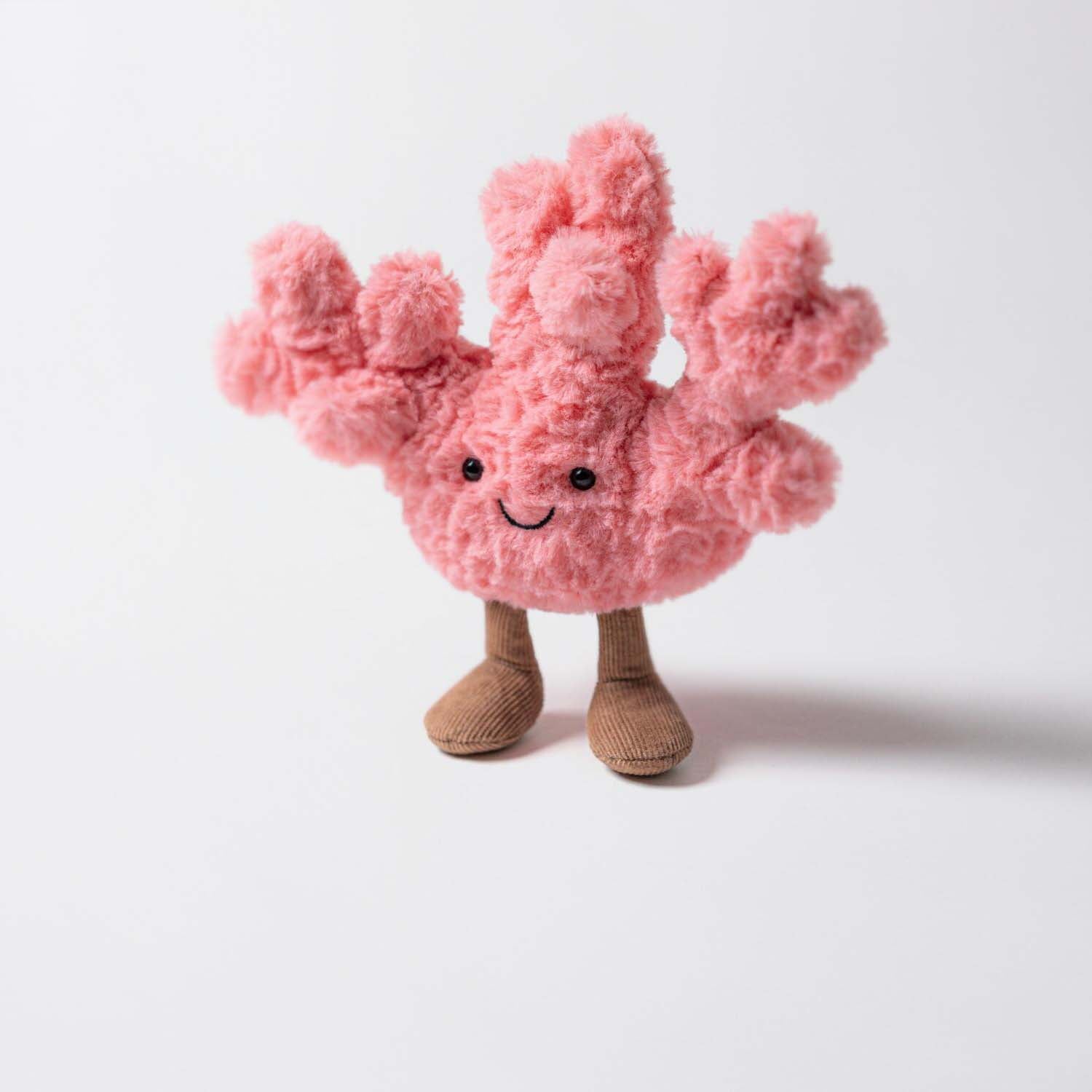 Kuscheltier Koralle aus rosa Plüsch mit lächelndem Gesicht, schwarzen Augen und braunen Beinen