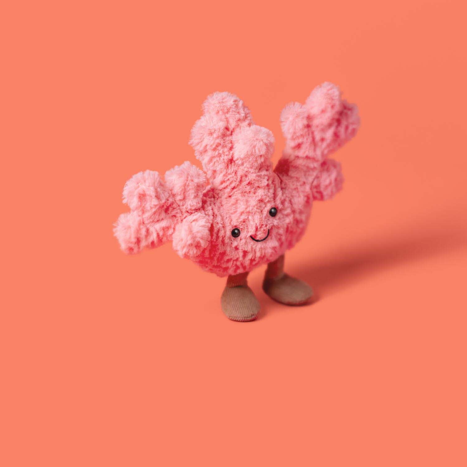 Kuscheltier Koralle, rosa Plüschtier mit lächelndem Gesicht, schwarzen Augen und braunen Füßen