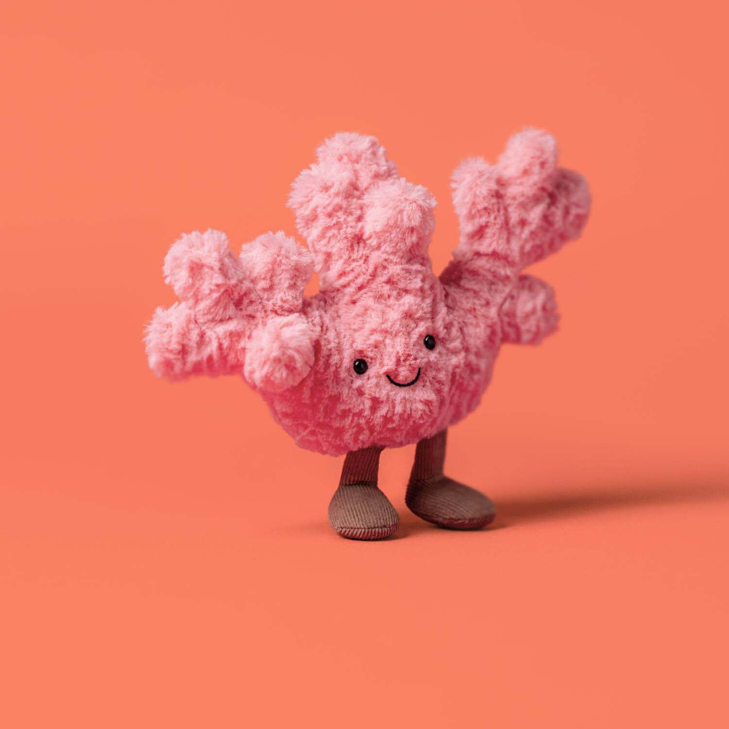 Kuscheltier Koralle, rosa Plüschfigur mit freundlichem Gesicht, schwarzen Augen und braunen Beinen