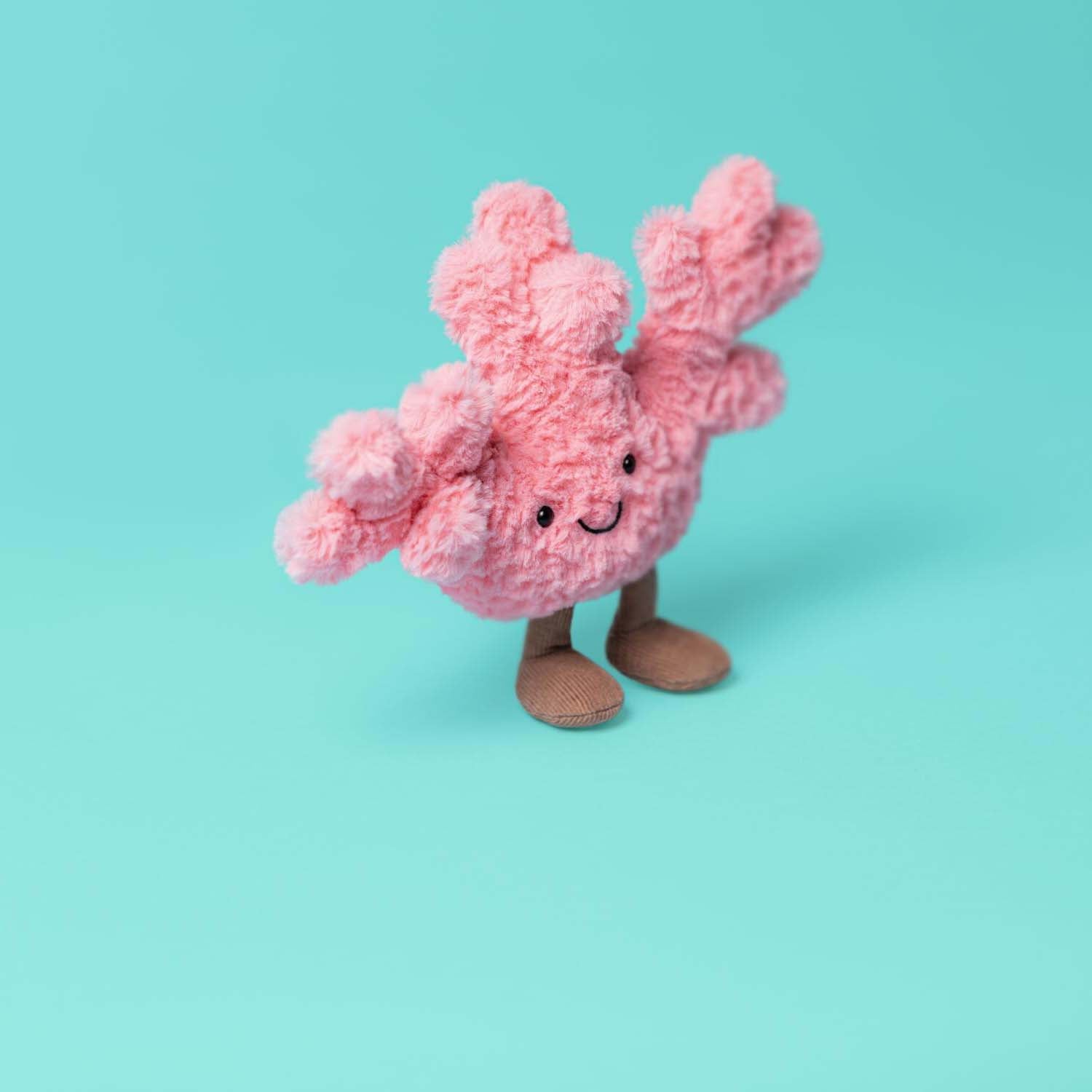 Kuscheltier Koralle, rosa Plüschtier mit lächelndem Gesicht und schwarzen Augen, aufrecht stehende Beine