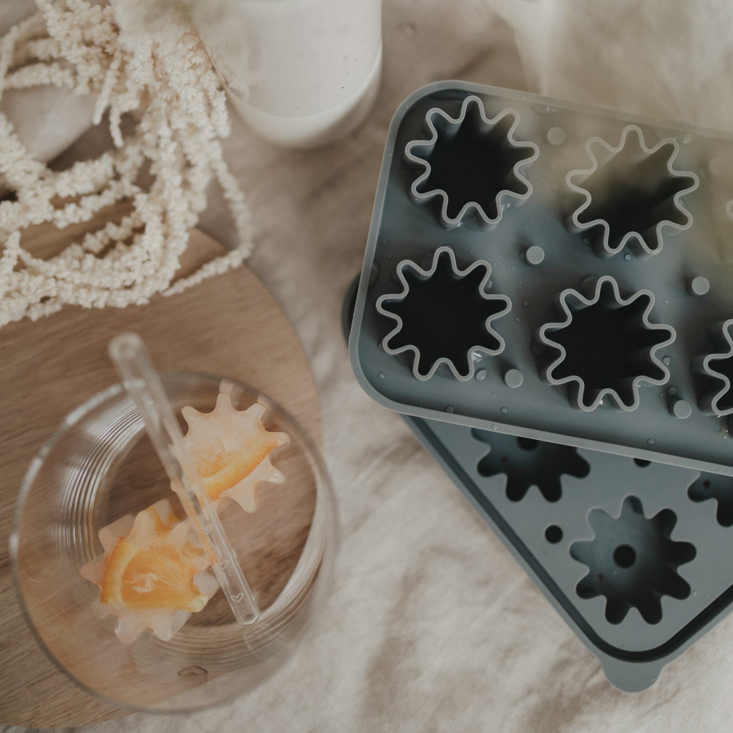 Eiswürfelform grau neben mehreren Blumen-Eiswürfeln in Dose und Glas