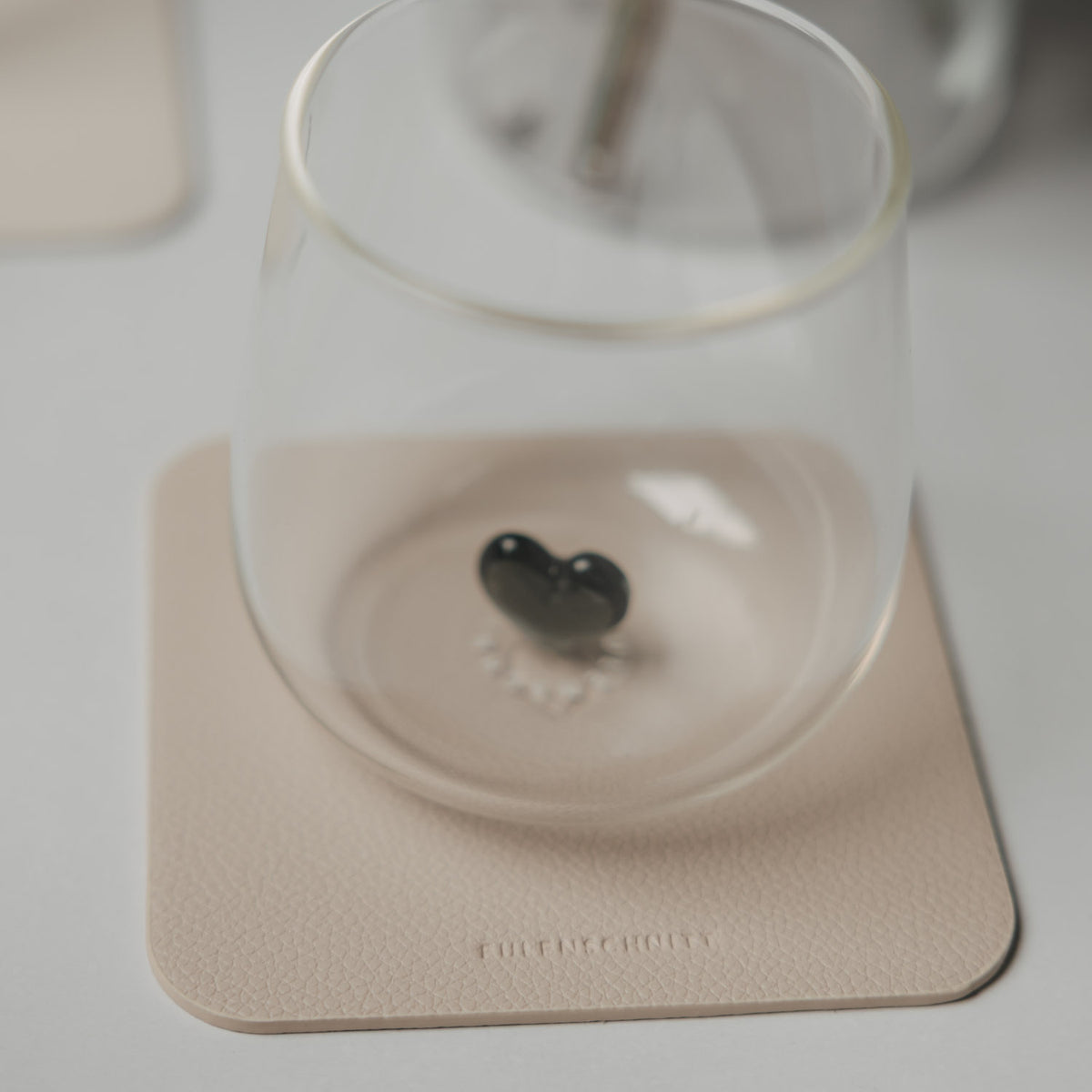 Beiger Untersetzer unter Glas mit Herz-Prägung
