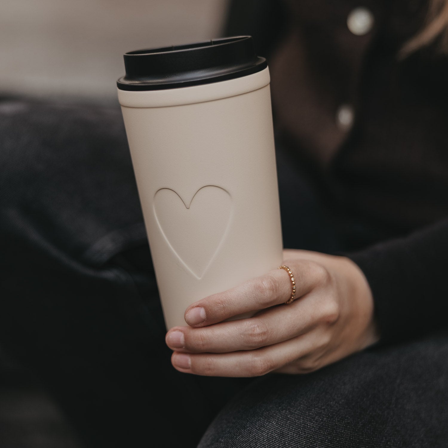 Cremefarbener To-go-Becher mit schwarzem Deckel und Herzrelief auf der Seite