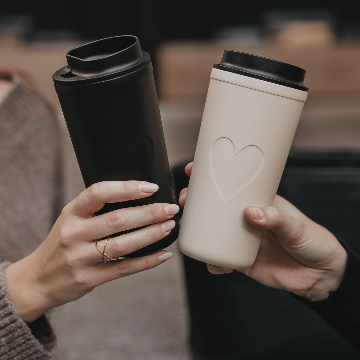 Cremefarbener To-go-Becher mit schwarzem Deckel und Herzrelief, seitlich gehalten