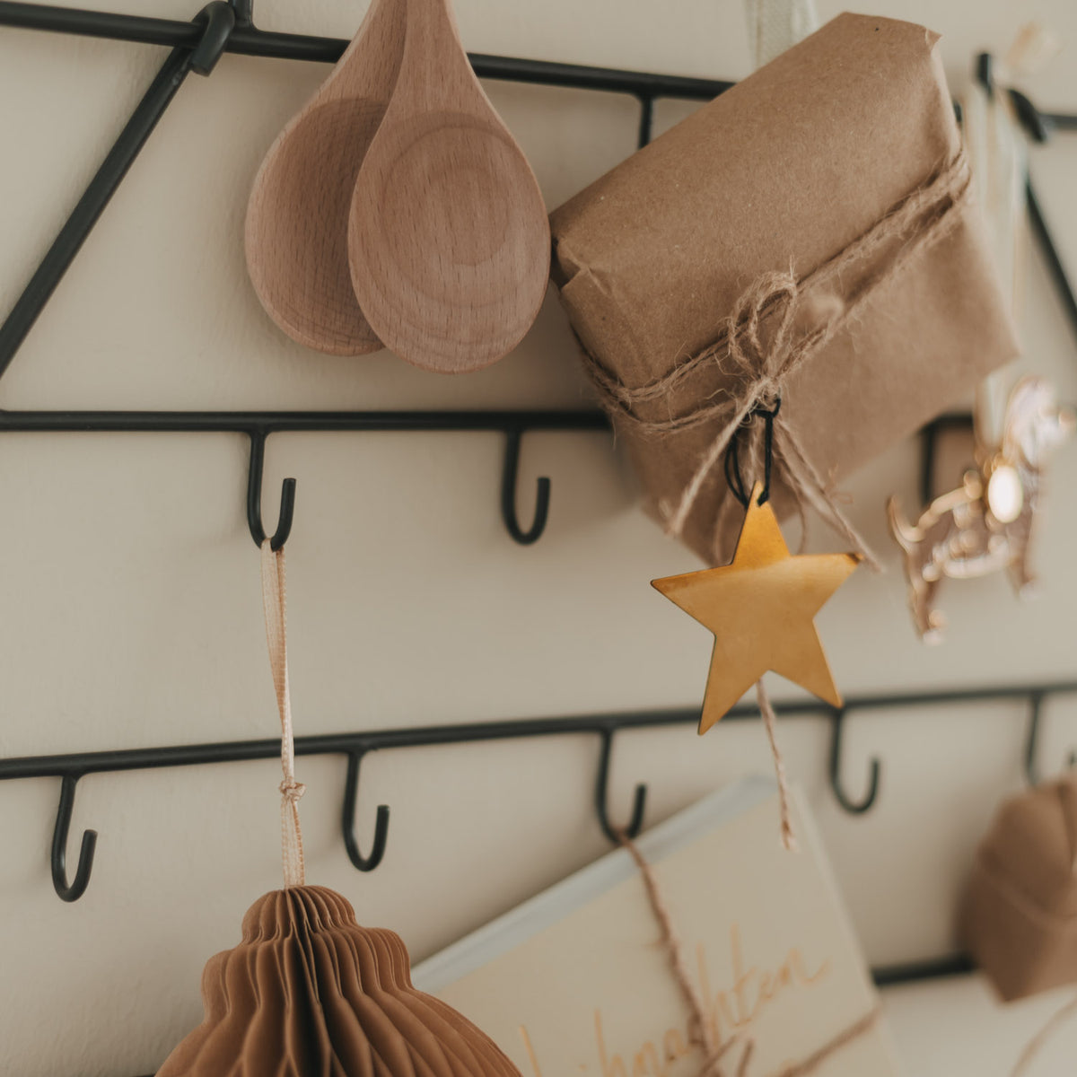 Nahaufnahme: Holz-Tropfenornamente, Sterne und kleine Geschenktüten am Metallrahmen